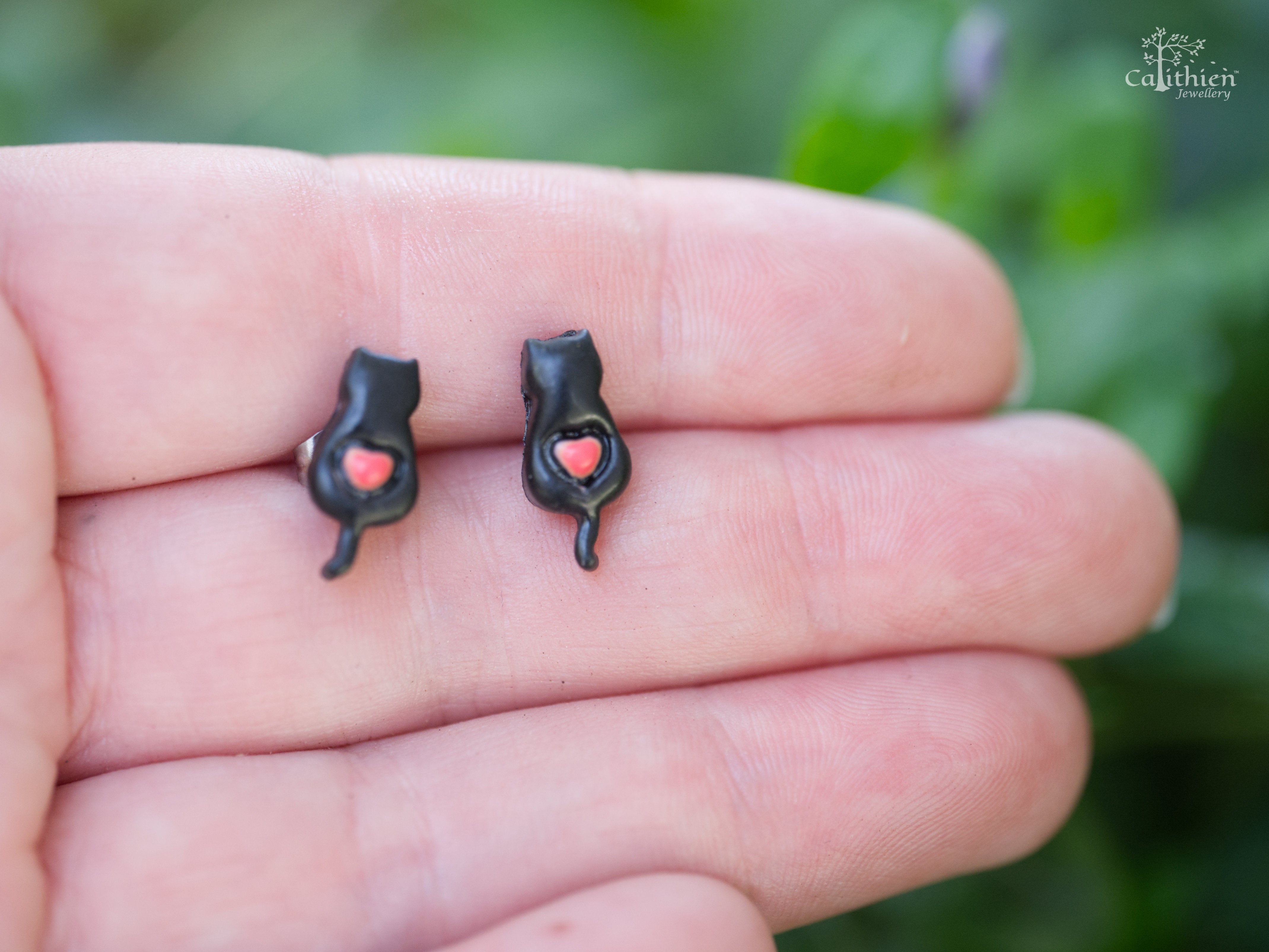 Pair of black cat stud earrings at true size on a hand to demonstrate size
