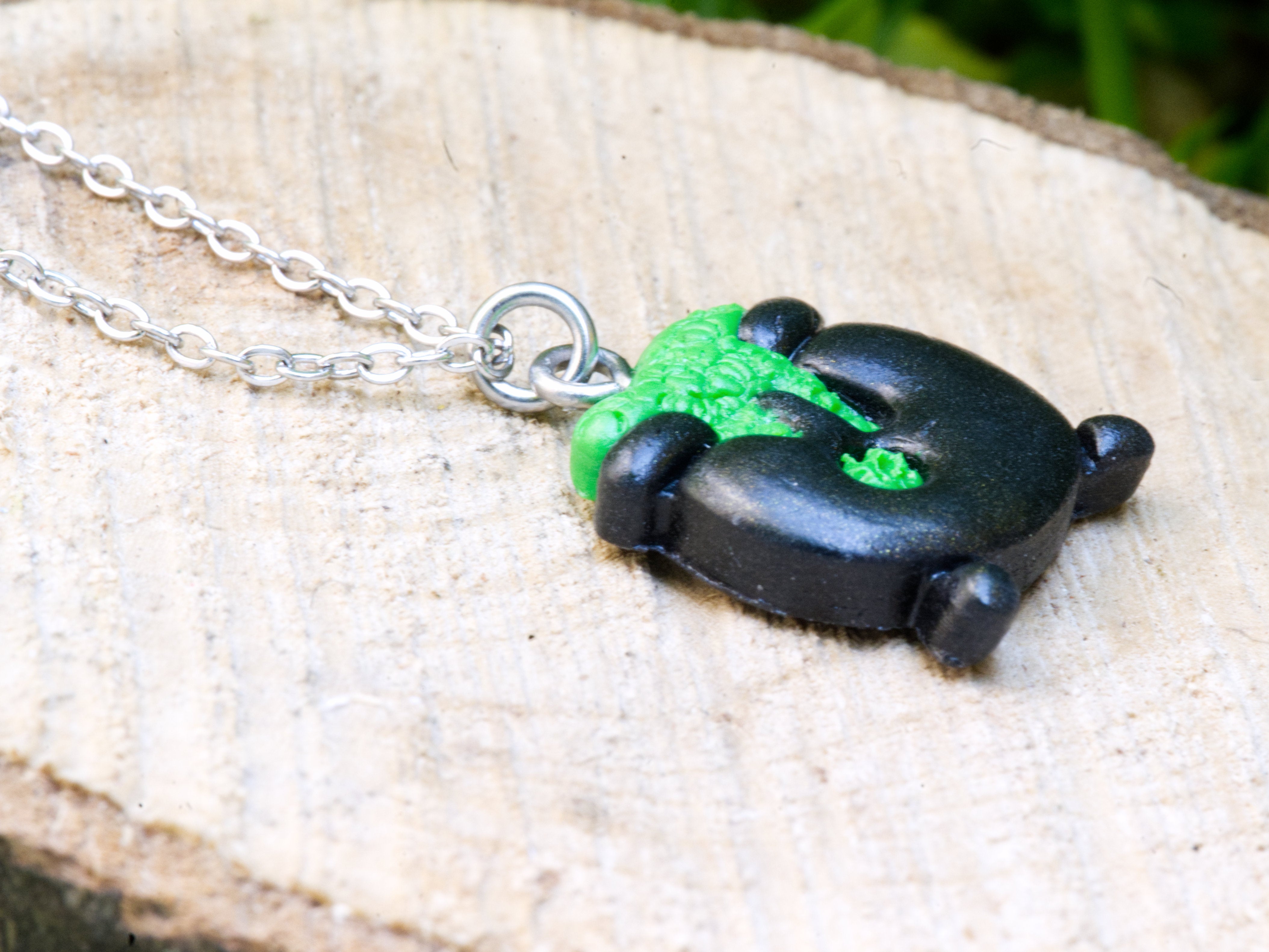 Close-up of black polymer clay cauldron pendant showing hand-sculpted green bubbling brew spilling over rim and three sculpted legs