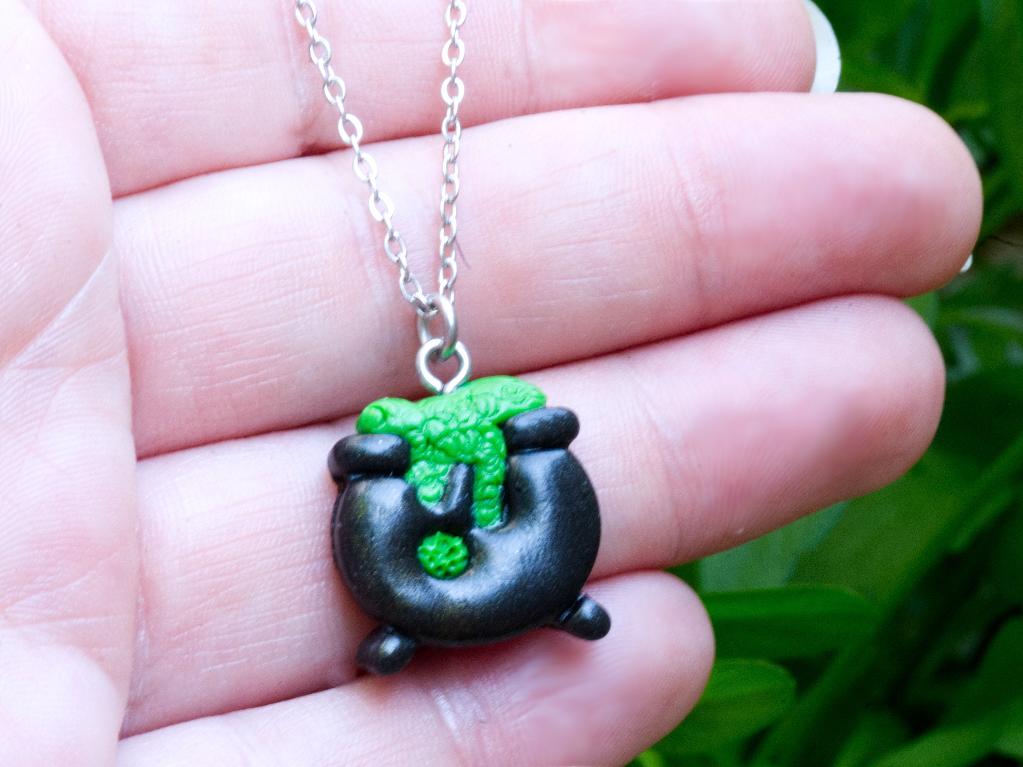 Black polymer clay cauldron necklace pendant on hand to demonstrate size