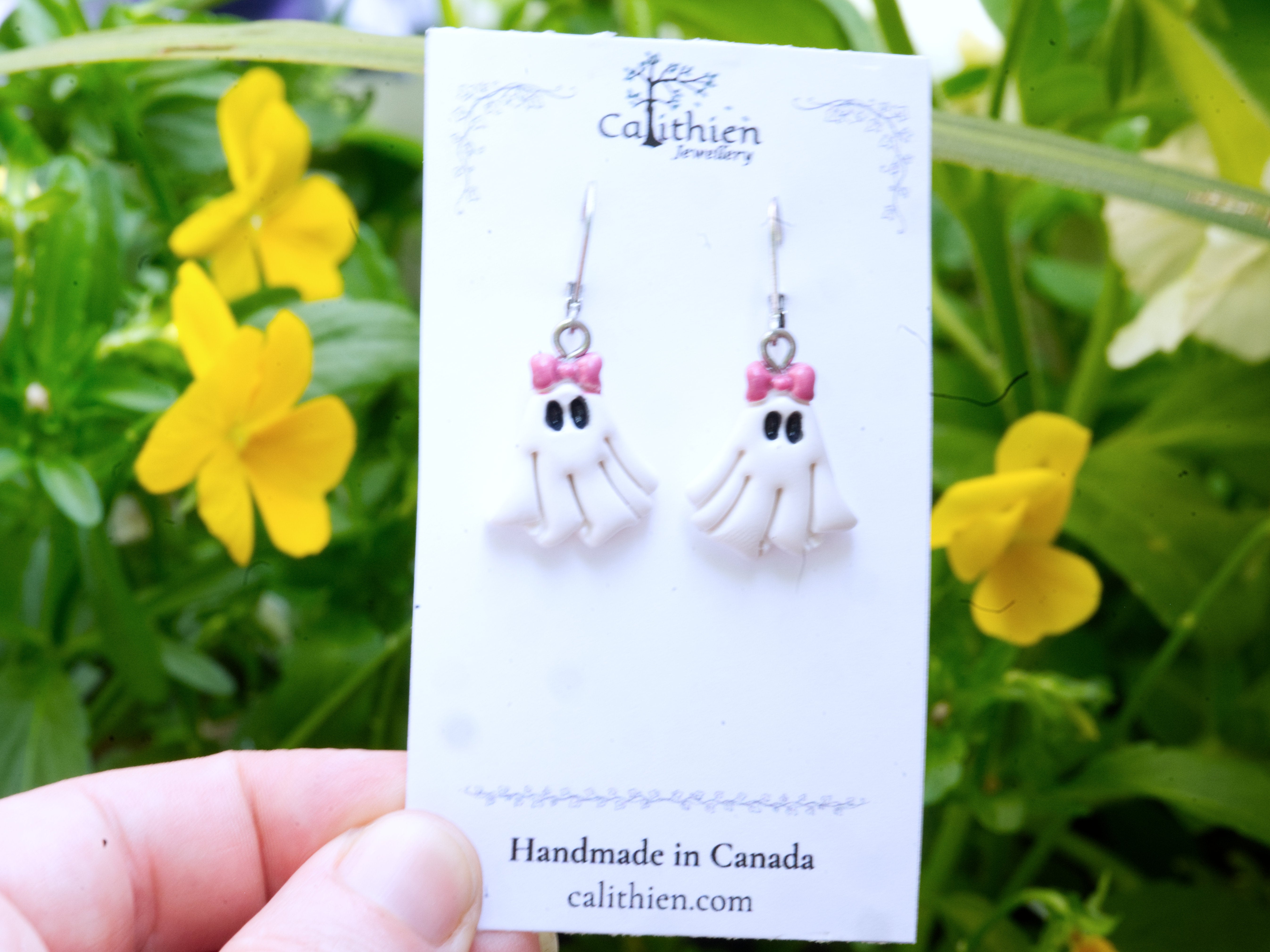Coquette ghost leverback earrings held in fingers on Calithien Jewellery branded display card reading Handmade in Canada