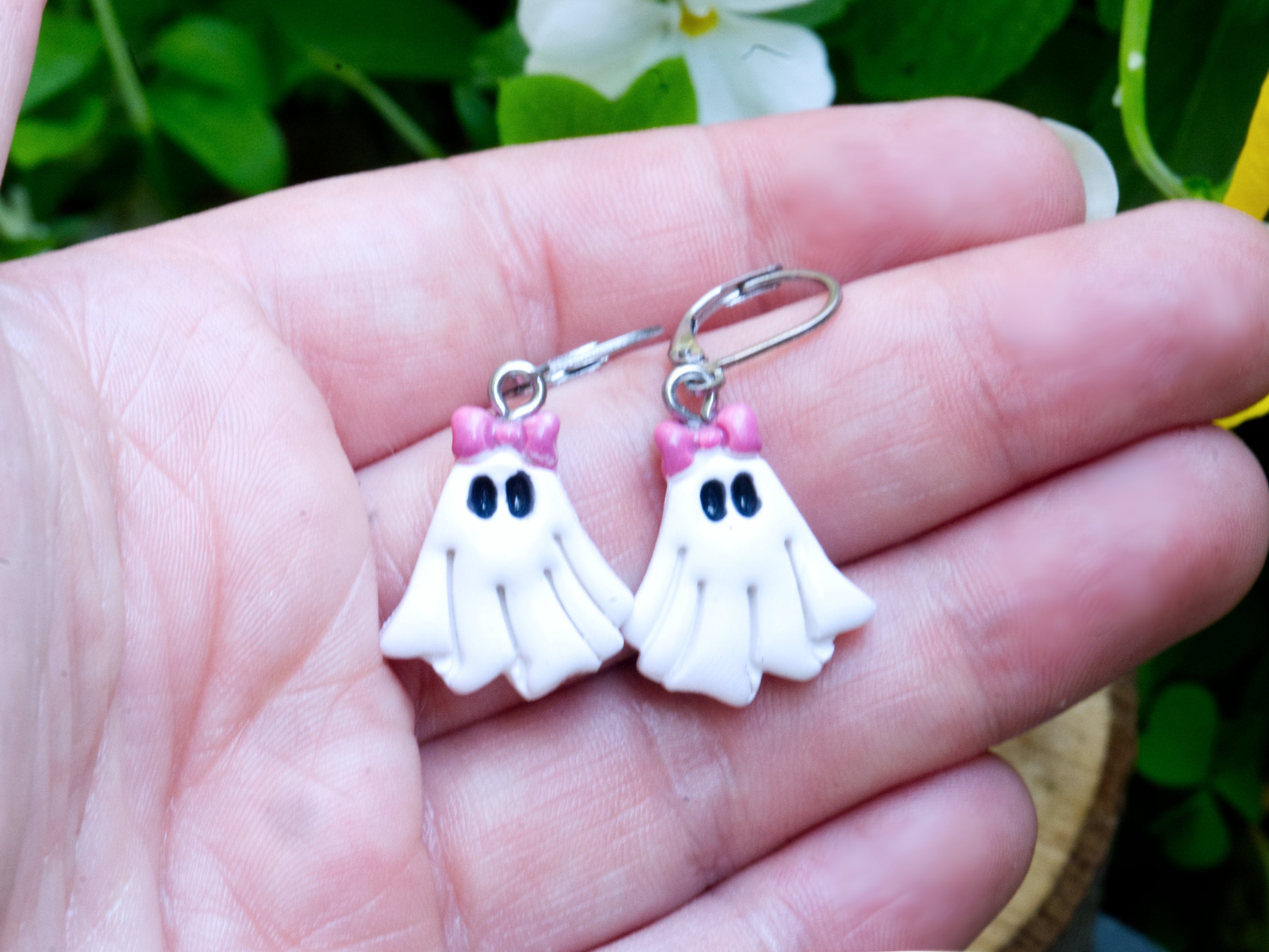 White polymer clay coquette ghost earrings held on hand to demonstrate size