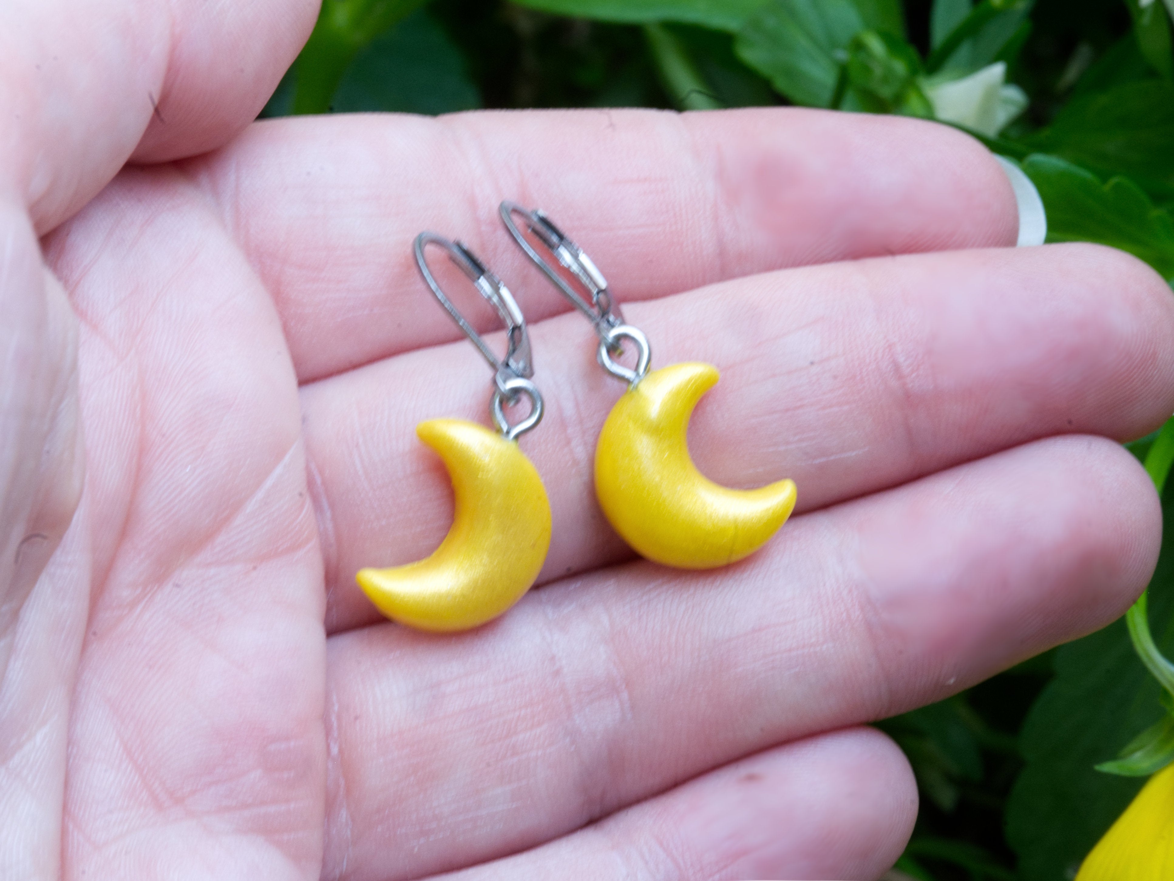 Gold shimmer crescent moon polymer clay earrings on hand to show scale