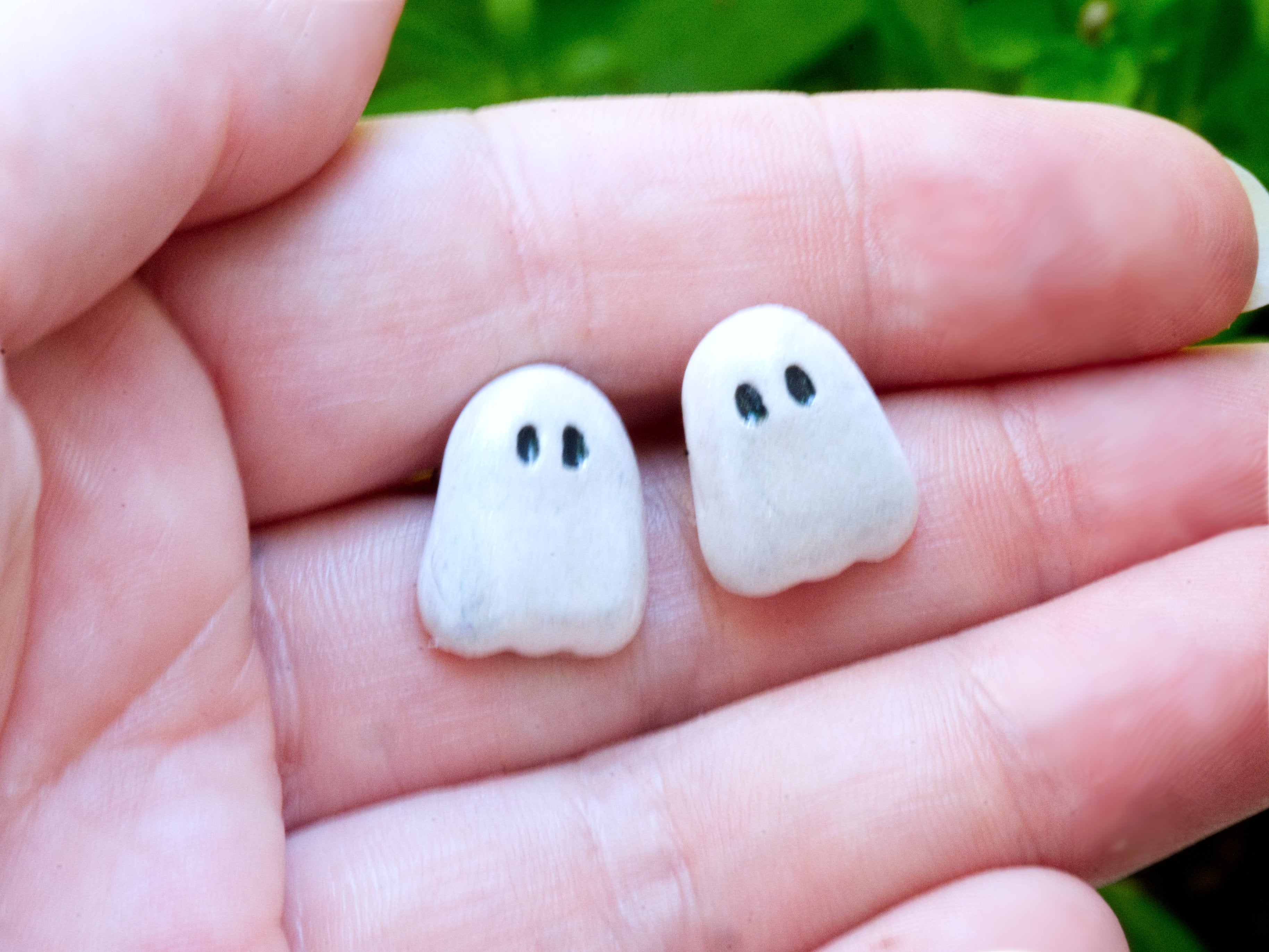 White polymer clay ghost stud earrings on hand to demonstrate size