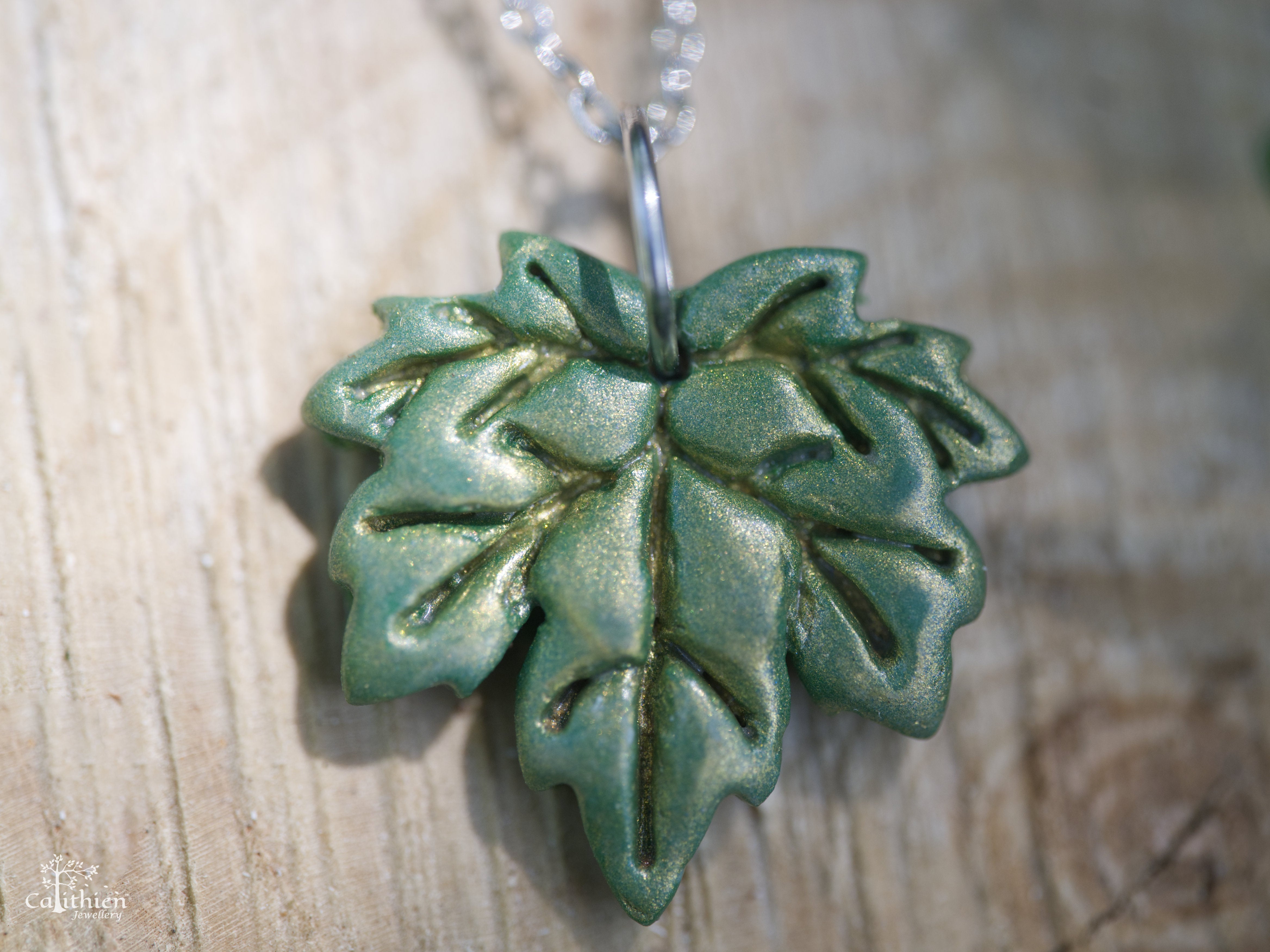 Close-up of green golden shimmer polymer clay maple leaf pendant showing hand-sculpted vein detail and light-catching shimmer finish