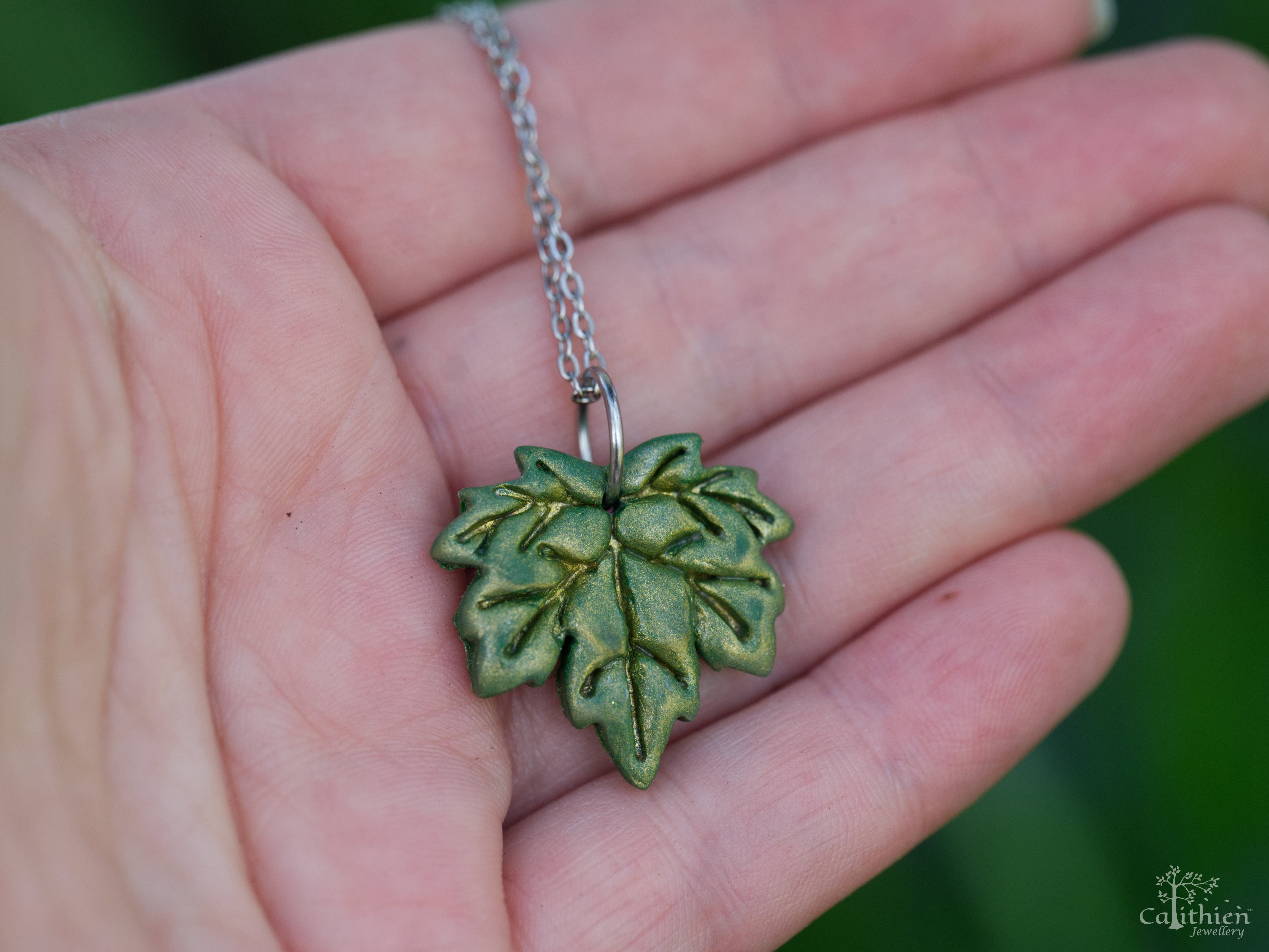Green maple leaf polymer clay pendant on fingers to demonstrate size