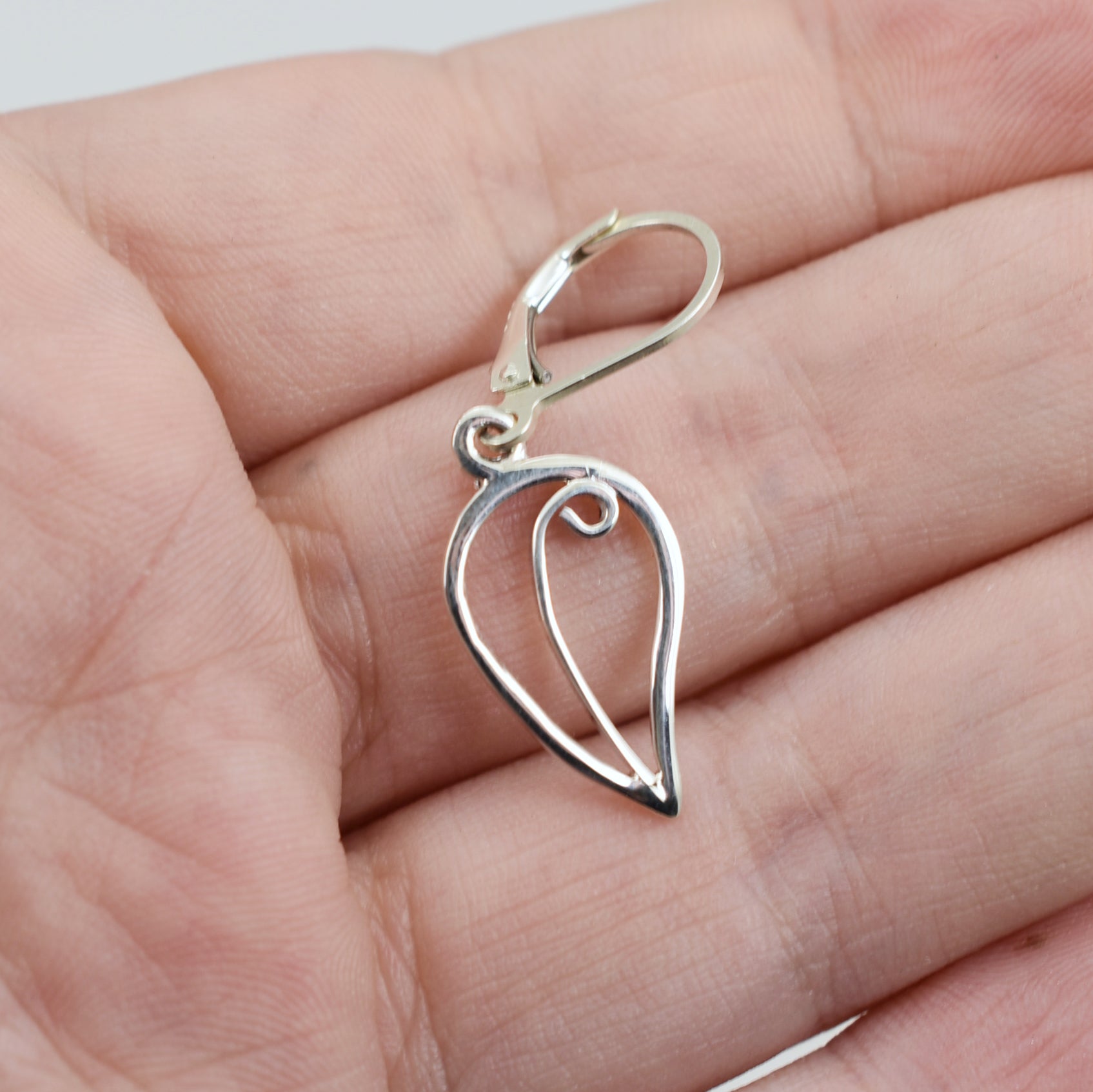 Handmade sterling silver leaf drop earrings with central swirl on a hand for sizing comparison