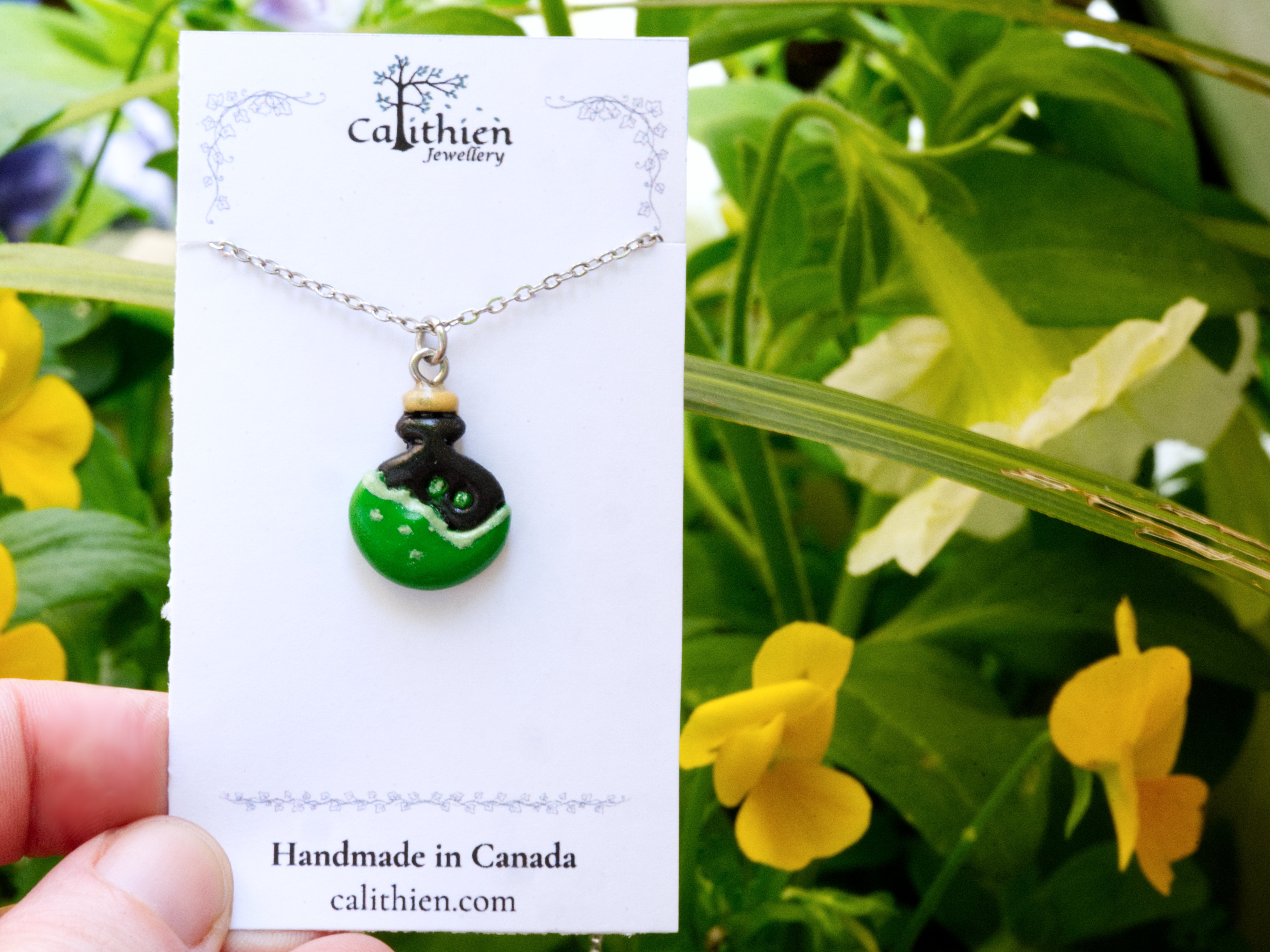 Potion bottle pendant necklace held in fingers on Calithien Jewellery branded display card reading Handmade in Canada