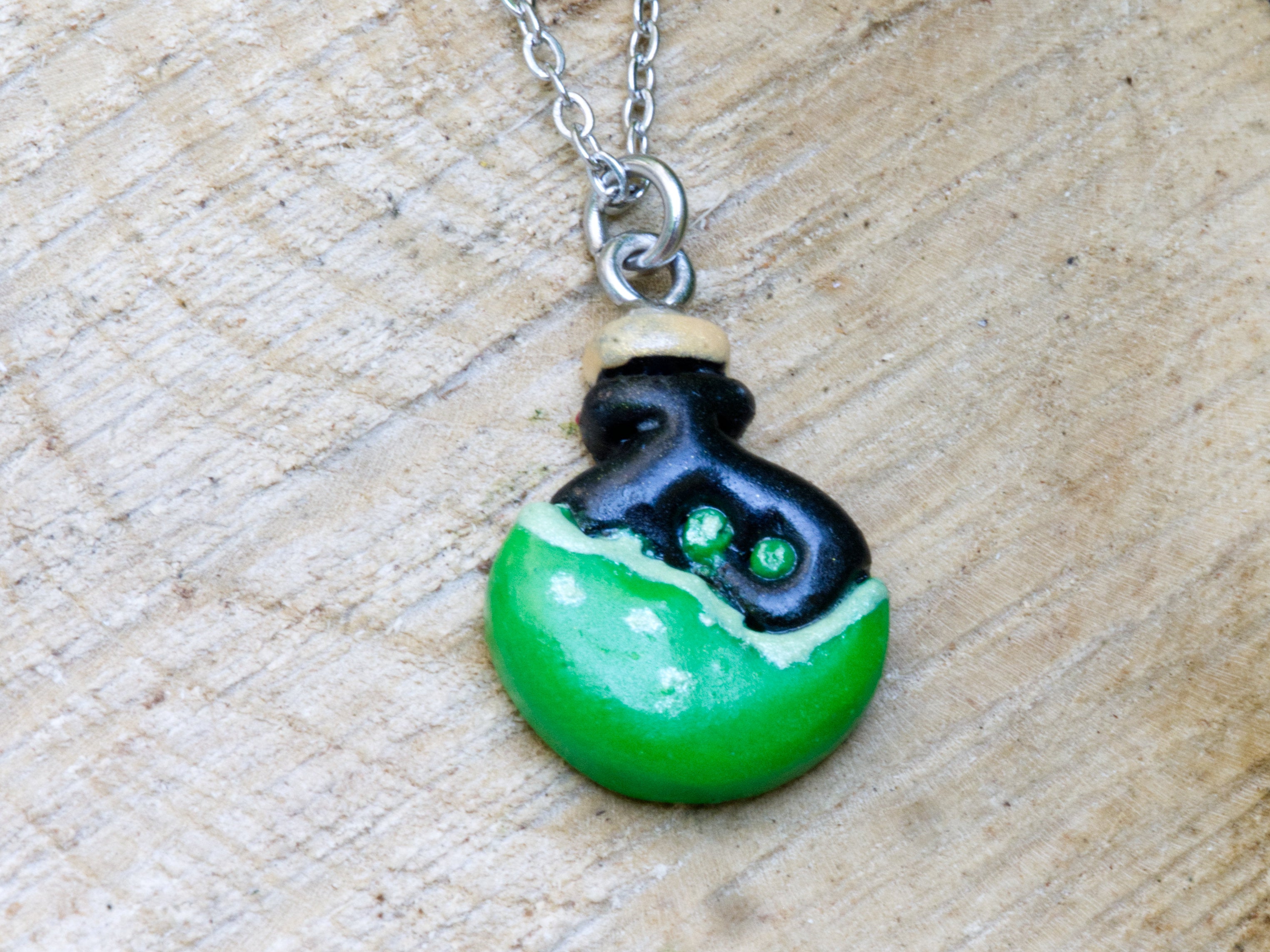 Handmade green and black polymer clay potion bottle pendant necklace with beige stopper on 304 stainless steel chain on natural wood surface