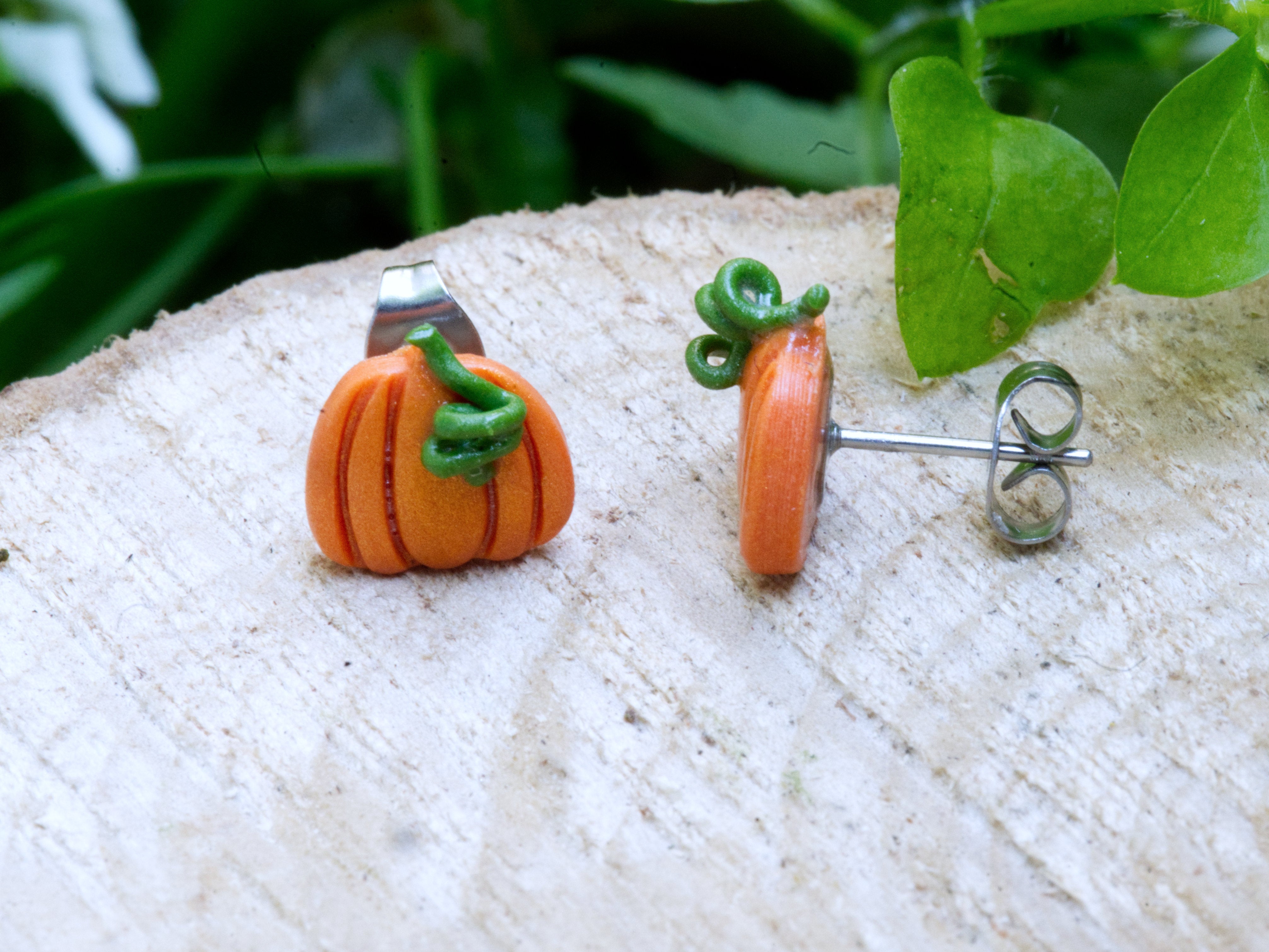 Close-up of orange polymer clay pumpkin stud earring showing ribbing, warm shimmer finish, and green clay stem and leaf