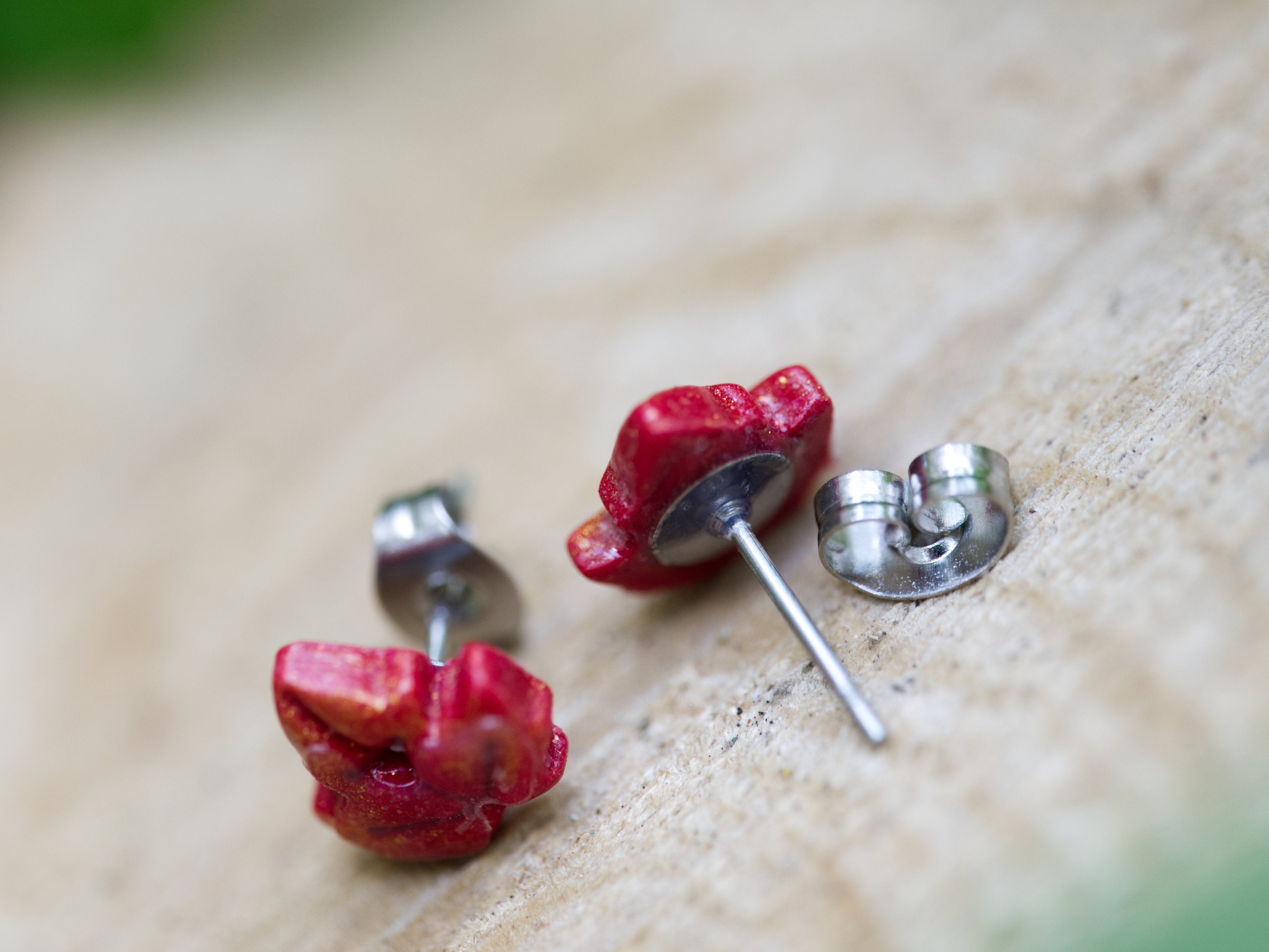 Close-up of the back of red and gold shimmer maple leaf stud earrings perched on weathered tree bark with blurred green forest background