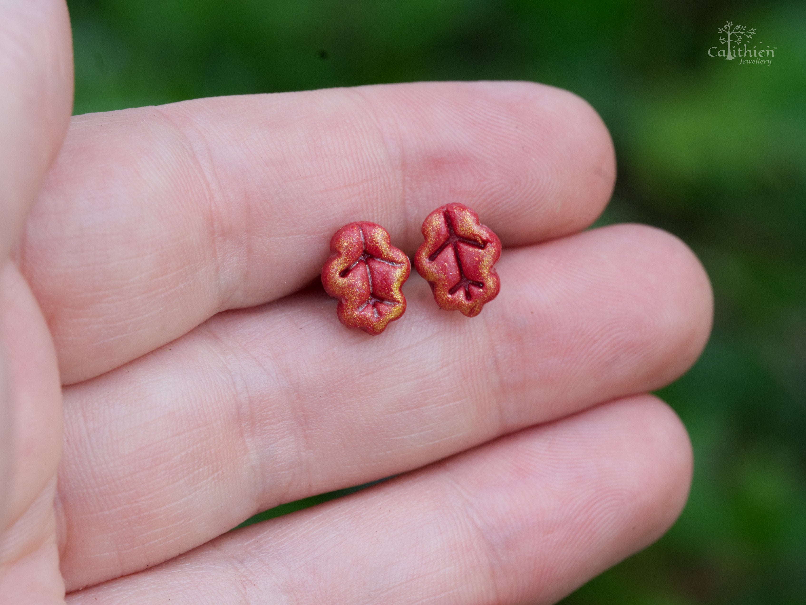 Polymer clay oak leaf stud earrings on a hand to demonstrate size