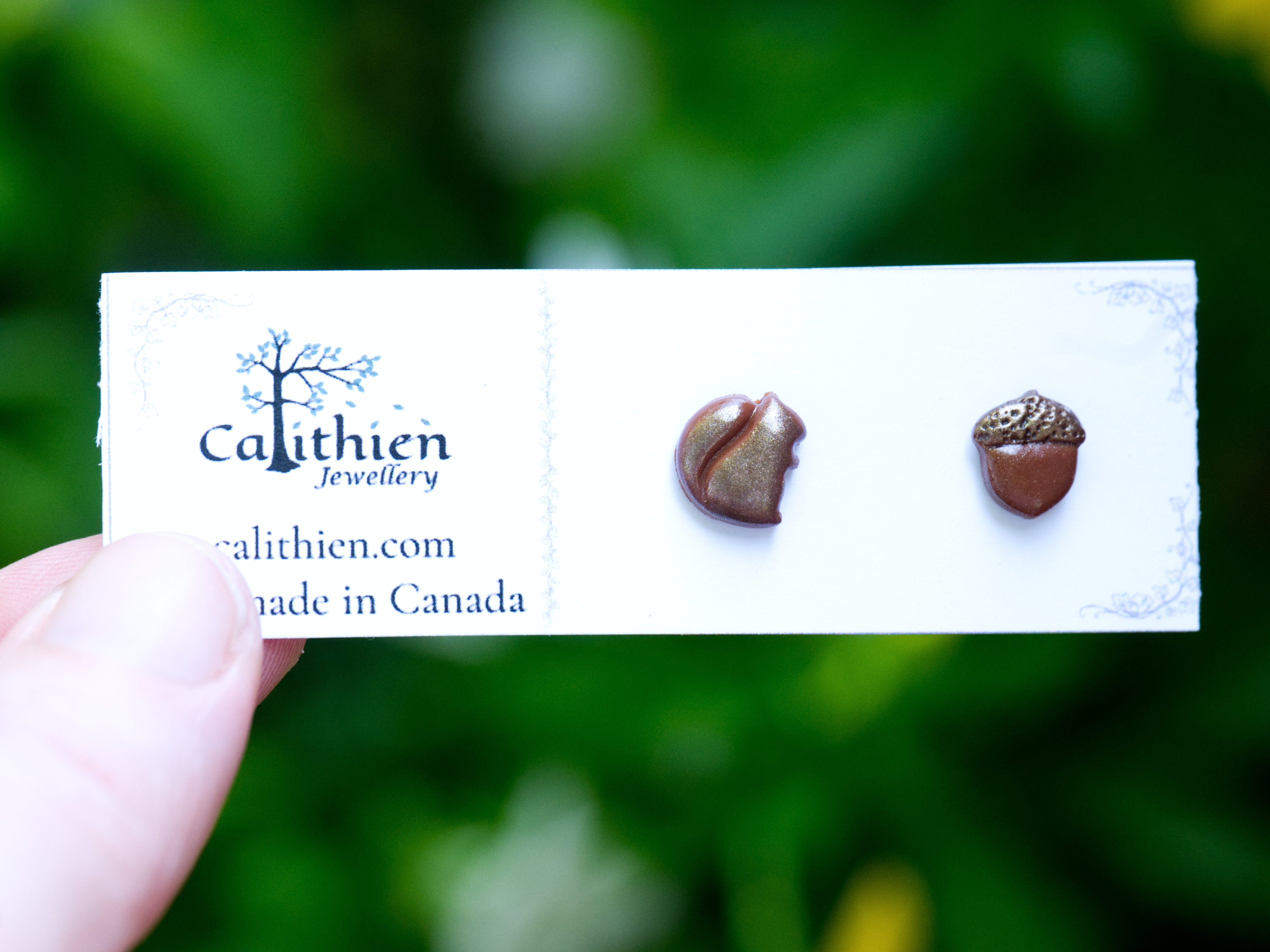 Mismatched squirrel and acorn stud earrings held in fingers on Calithien Jewellery branded display card reading Handmade in Canada