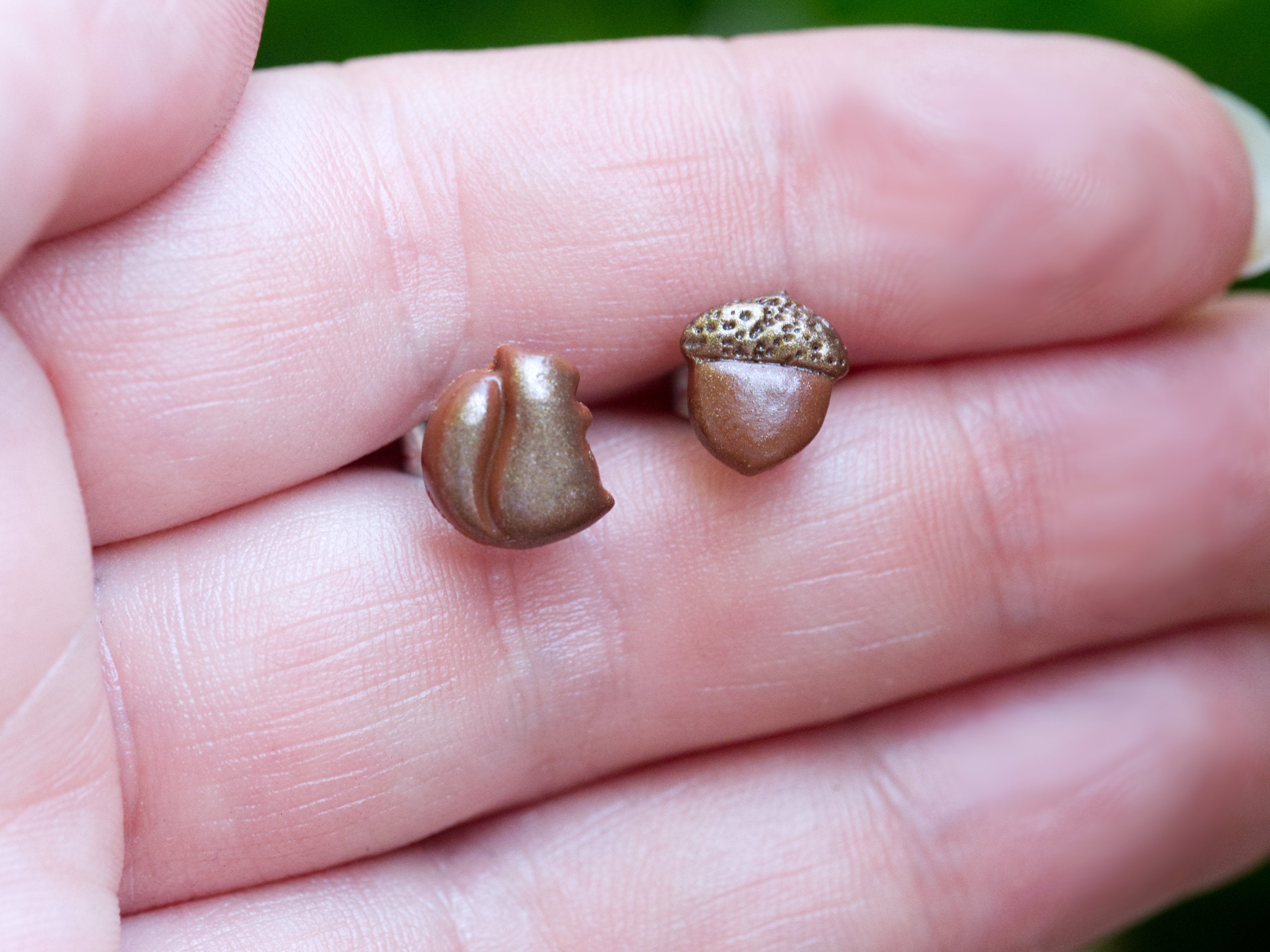 Brown polymer clay squirrel and acorn stud earrings on hand to demonstrate size