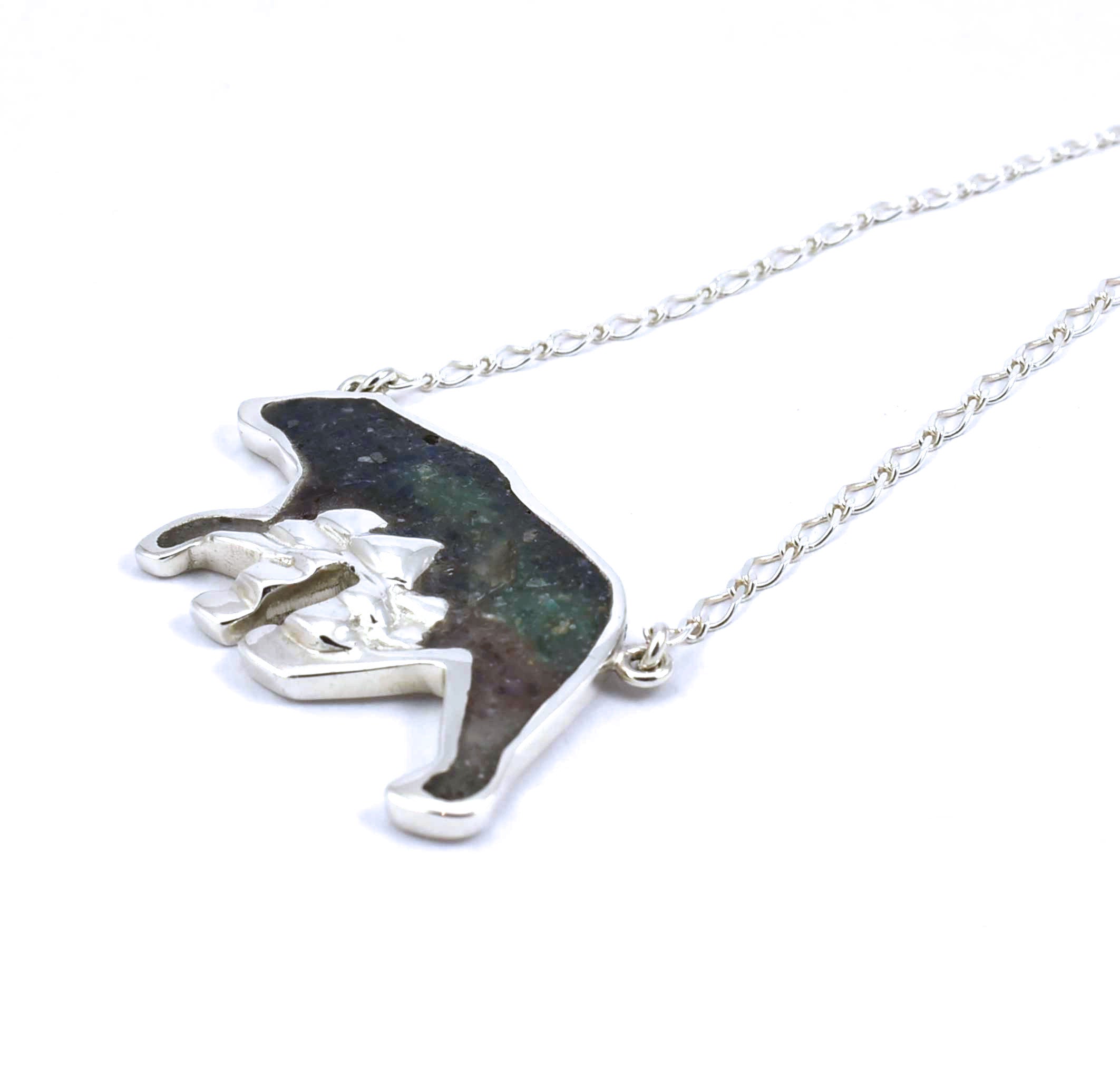 Right side view of large sterling silver bear pendant with tree accents and crushed gemstone inlay