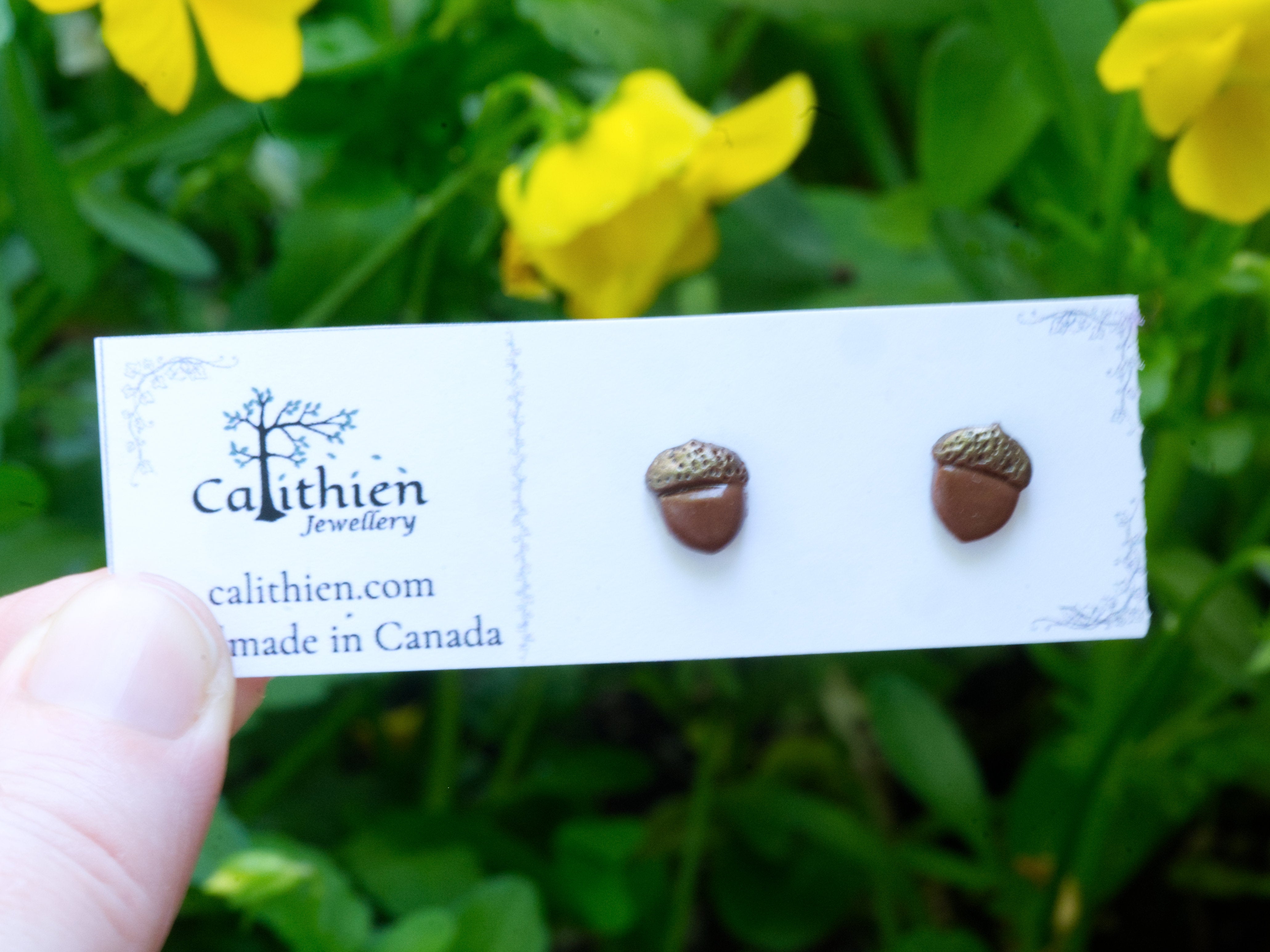 Acorn stud earrings held in fingers on Calithien Jewellery branded display card reading Handmade in Canada