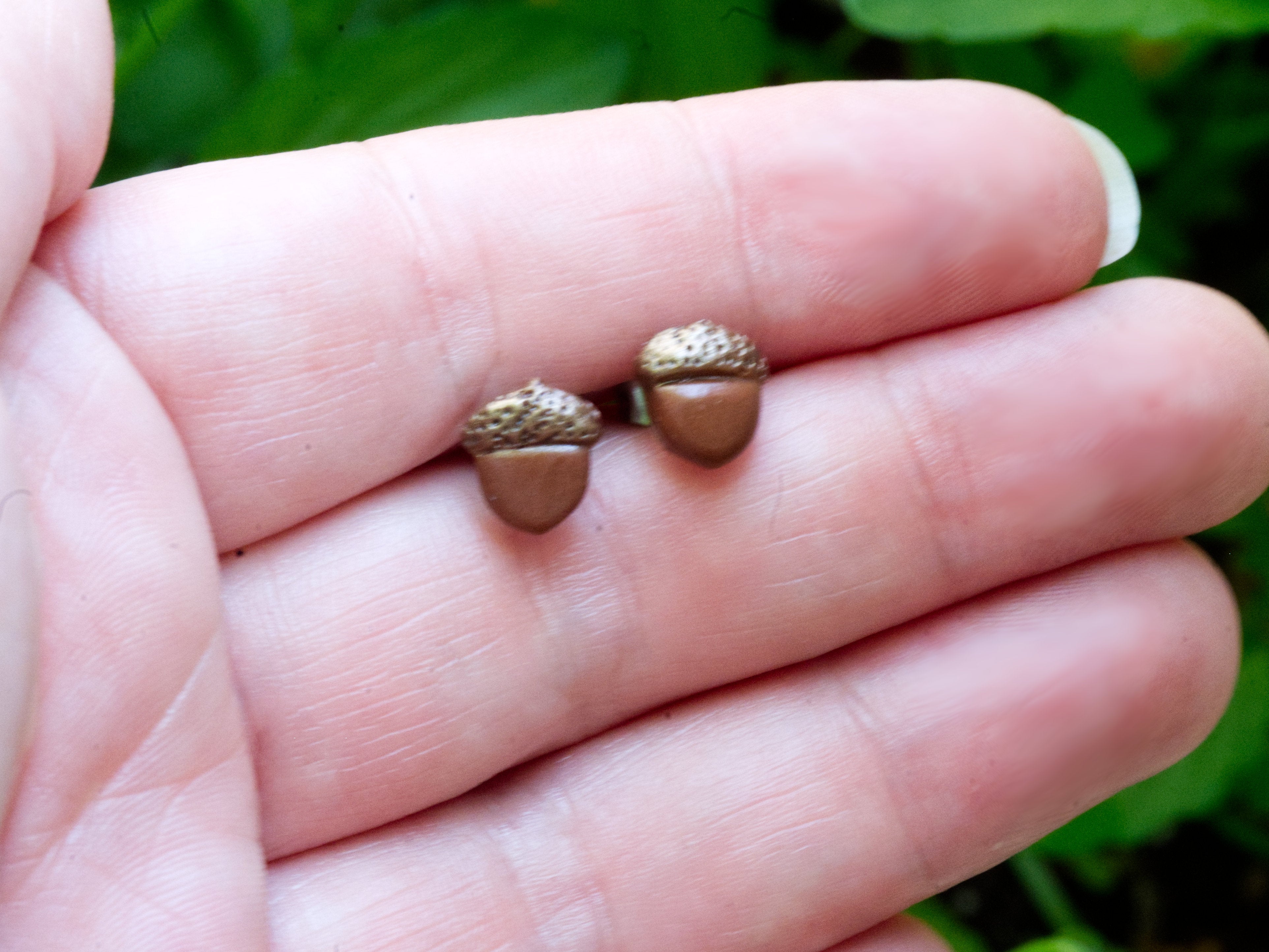 Brown polymer clay acorn stud earrings on fingers to demonstrate size