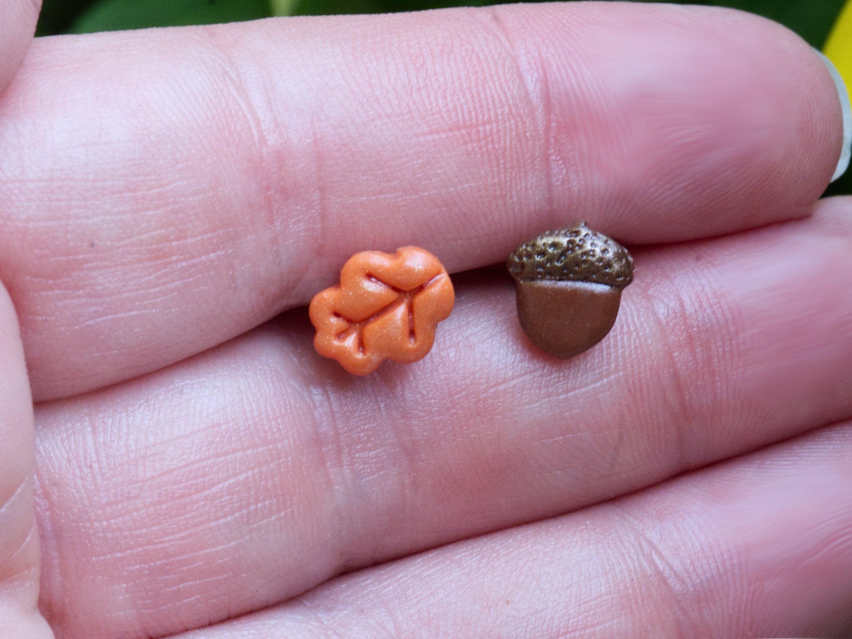 Orange oak leaf and brown acorn polymer clay stud earrings on hand to demonstrate size