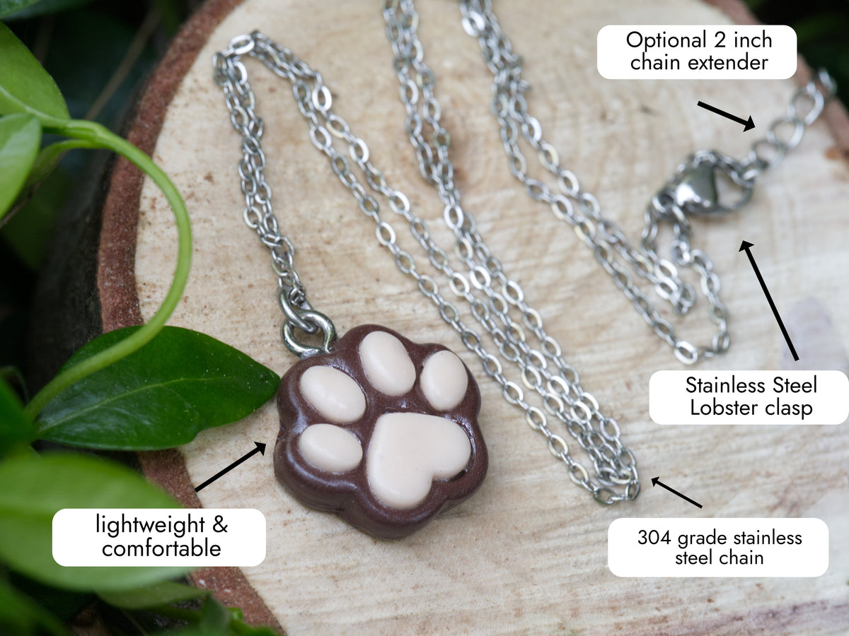 Brown paw print necklace with labelled details showing the stainless steel chain, optional 2-inch extender and lobster clasp.