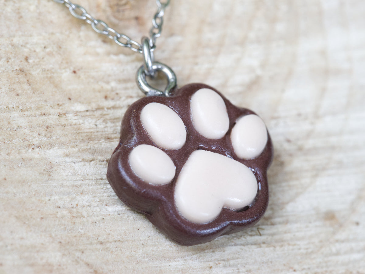 Close-up of the coffee-brown polymer clay paw print pendant with individually placed pink pads and a matte finish.