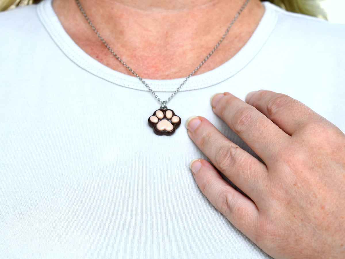 Handmade brown polymer clay paw print necklace worn against a white T-shirt, showing the pendant's size and everyday style.