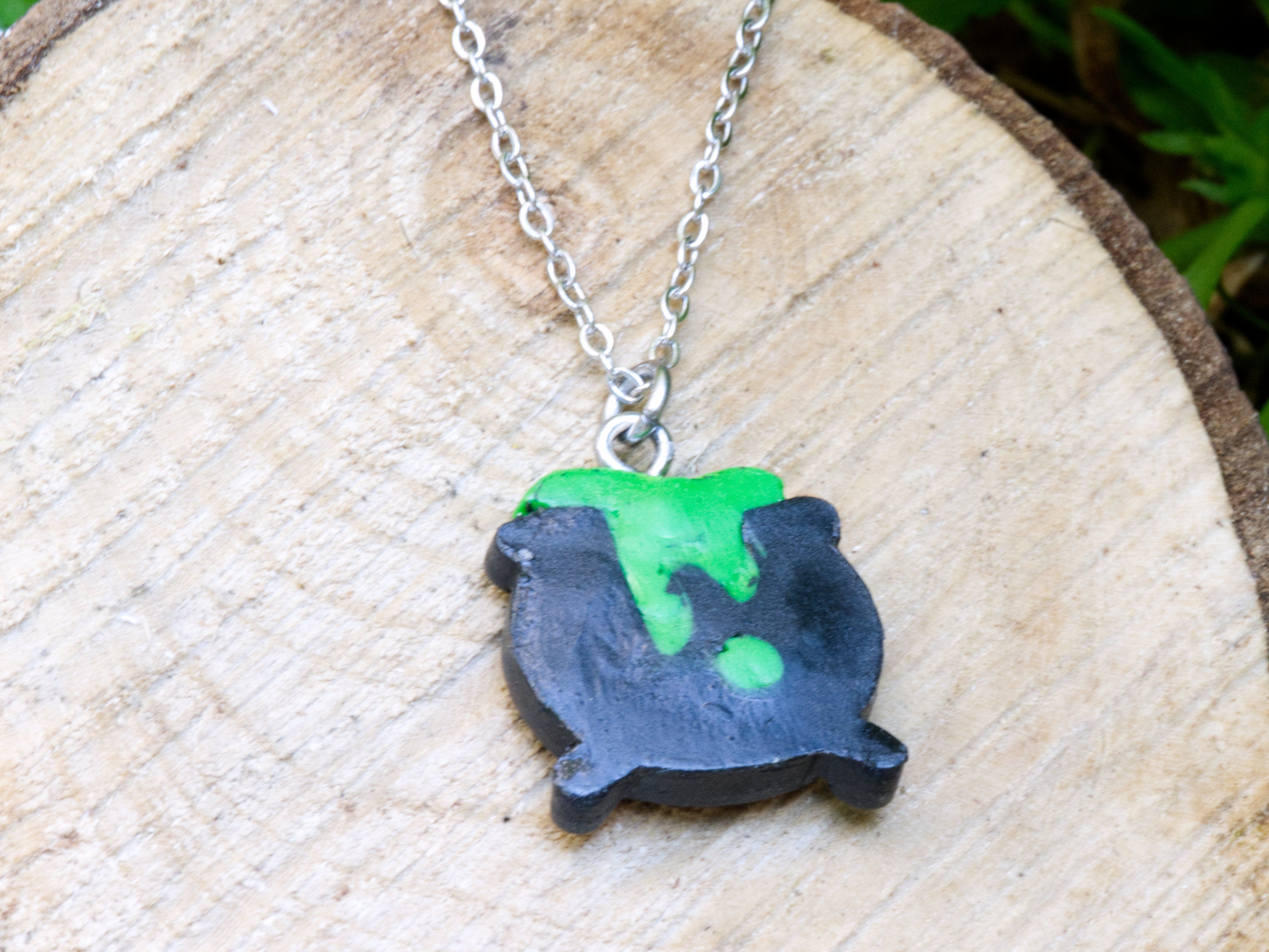 Back of black polymer clay cauldron pendant showing hand-sculpted green bubbling brew spilling over rim and three sculpted legs