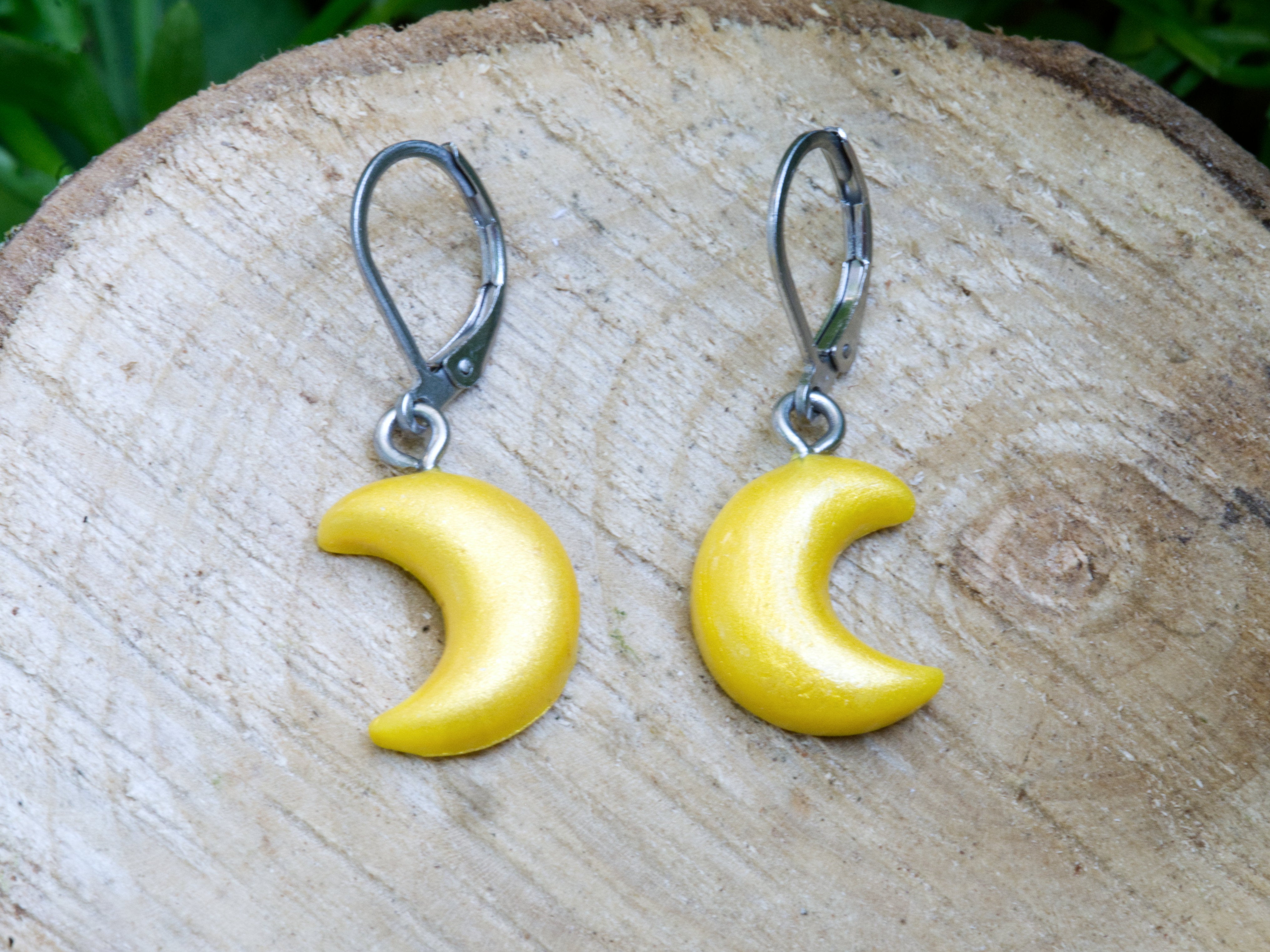 Handmade gold shimmer polymer clay crescent moon leverback earrings displayed on natural wood surface with garden flowers background