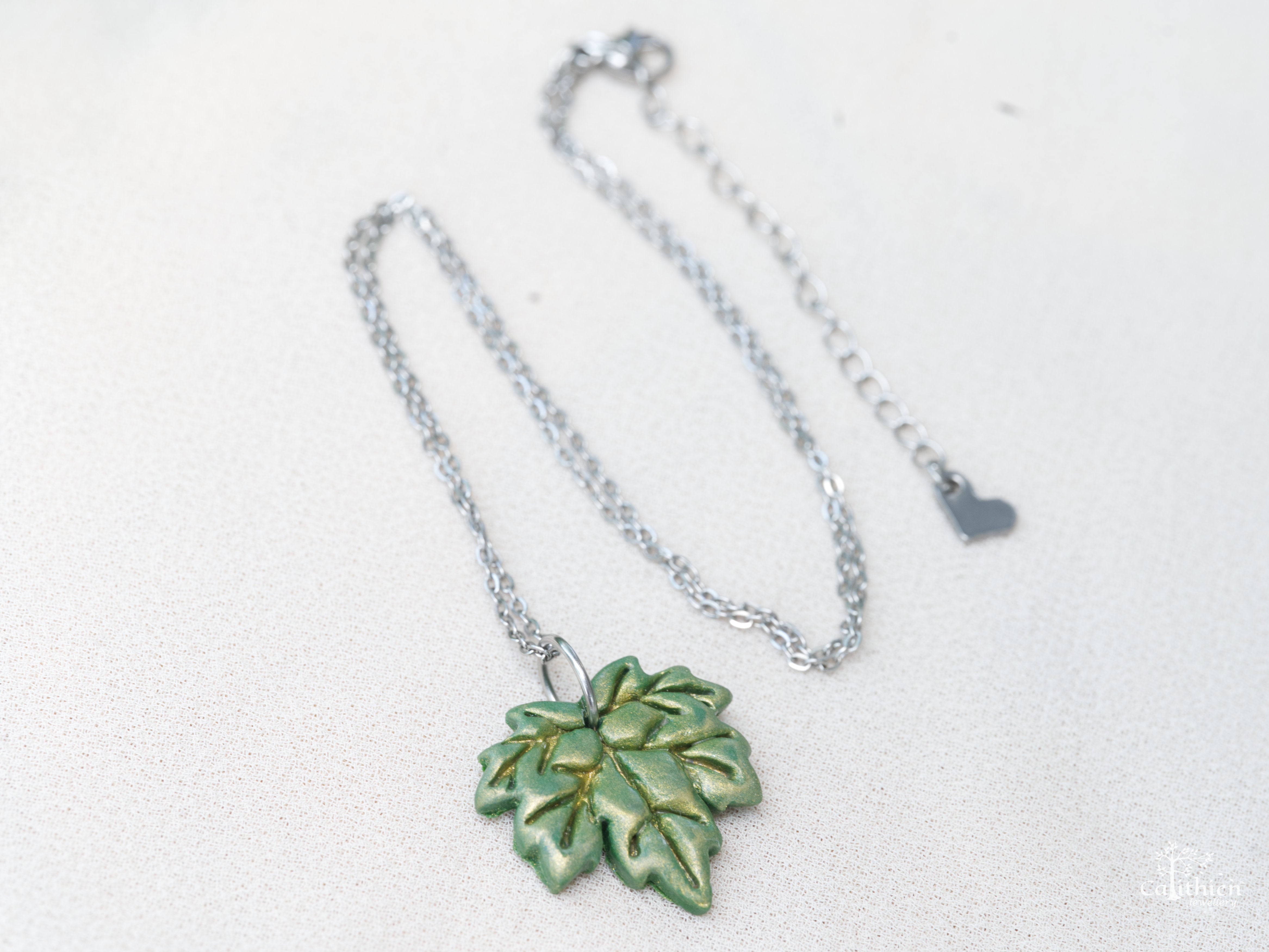 Green maple leaf necklace pendant catching light on fabric surface displaying full chain plus extender