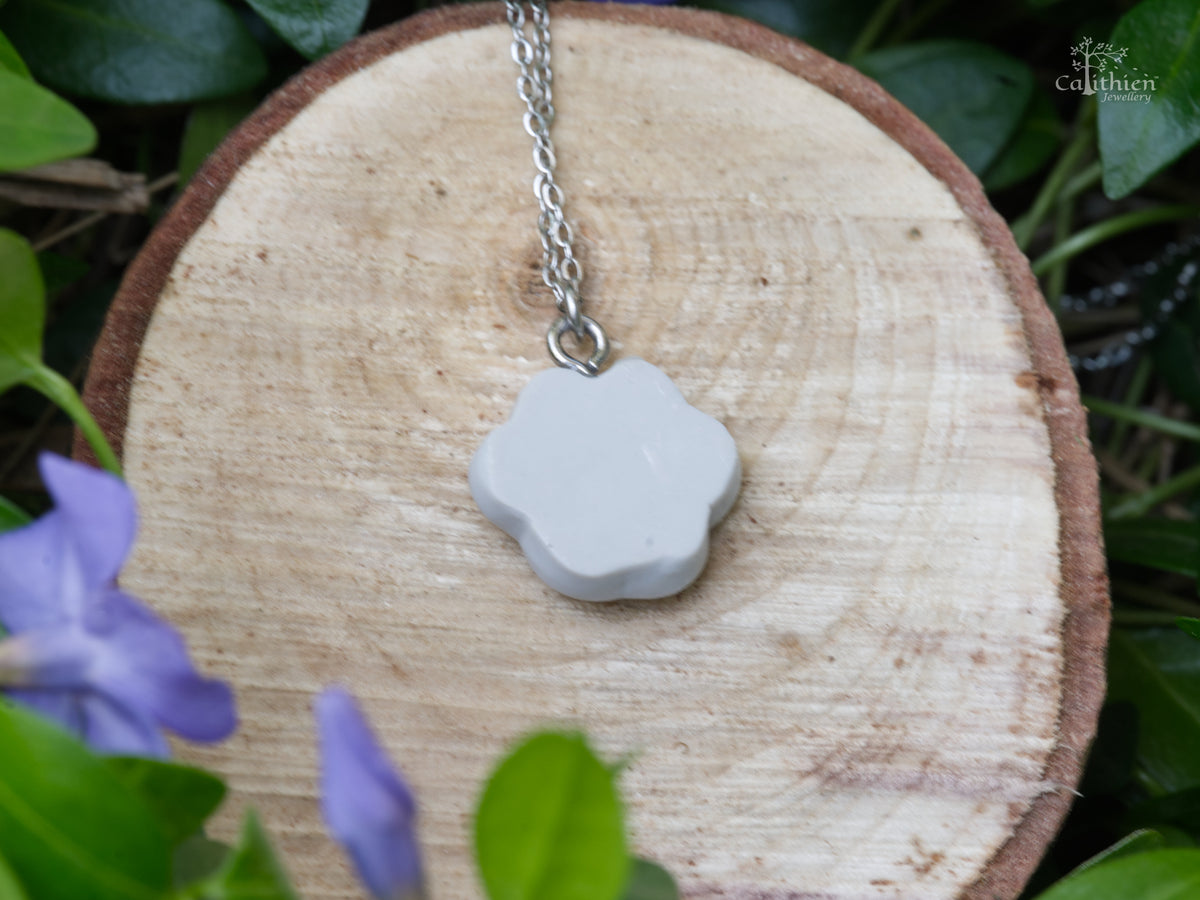 Back view of the handmade grey polymer clay paw print necklace pendant displayed on a natural wooden surface.