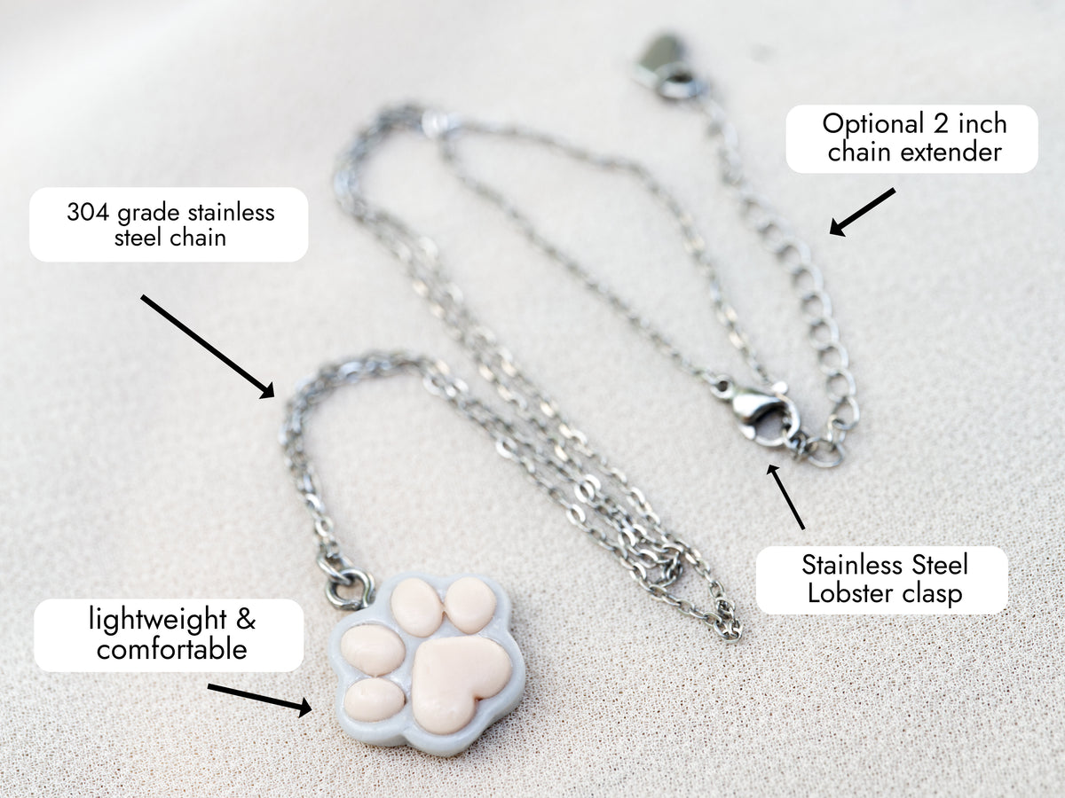 Grey paw print necklace with labelled details showing the stainless steel chain, optional 2-inch extender and lobster clasp.