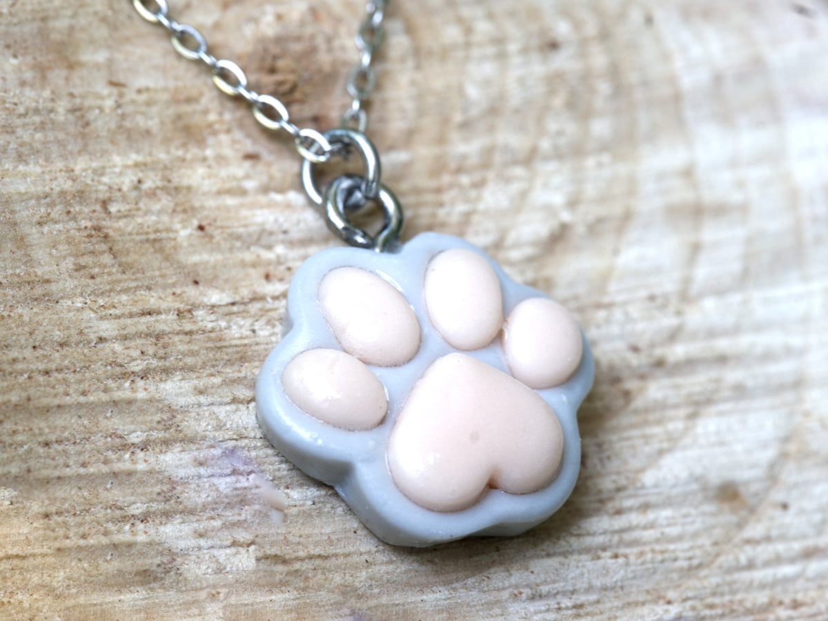 Close-up of the light dove-grey polymer clay paw print pendant with individually placed pink pads and a matte finish.