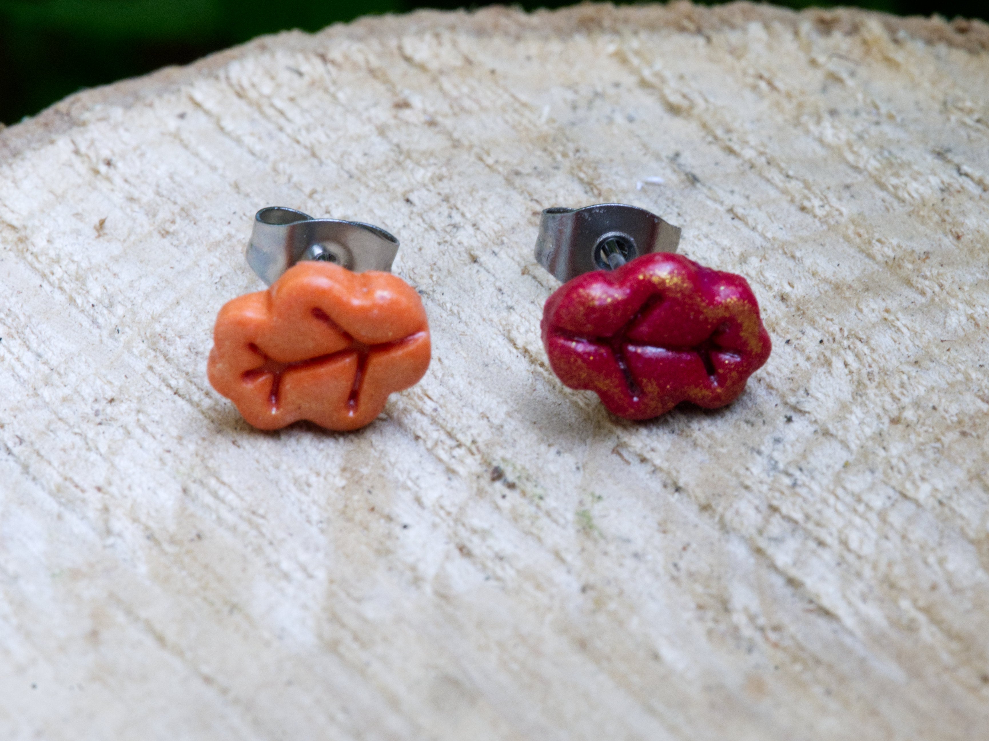 Close-up of mismatched red and orange polymer clay oak leaf stud earrings showing detail and shimmer finish