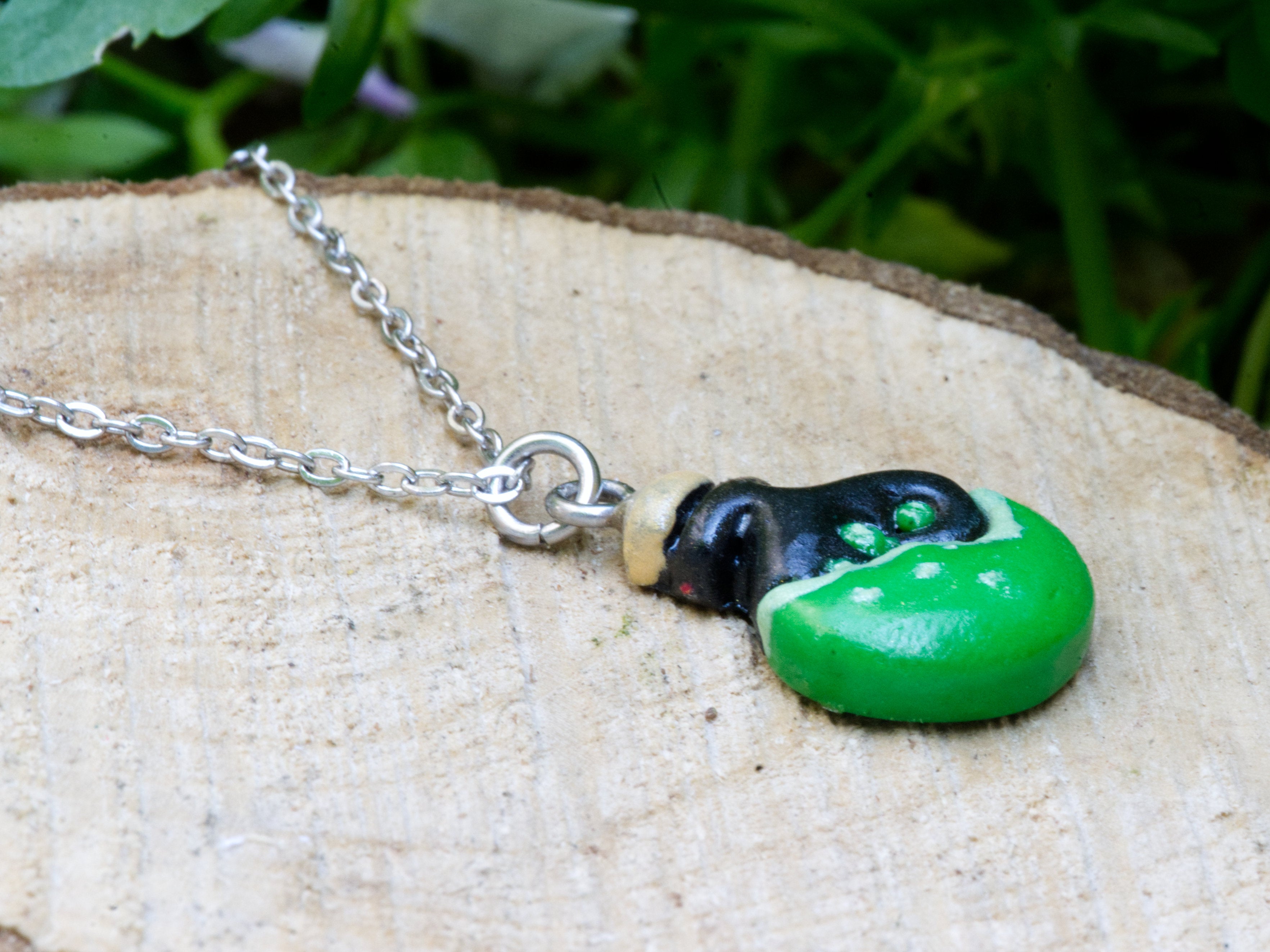 Close-up of polymer clay potion bottle pendant showing black body, green potion, beige stopper, and two green bubble details