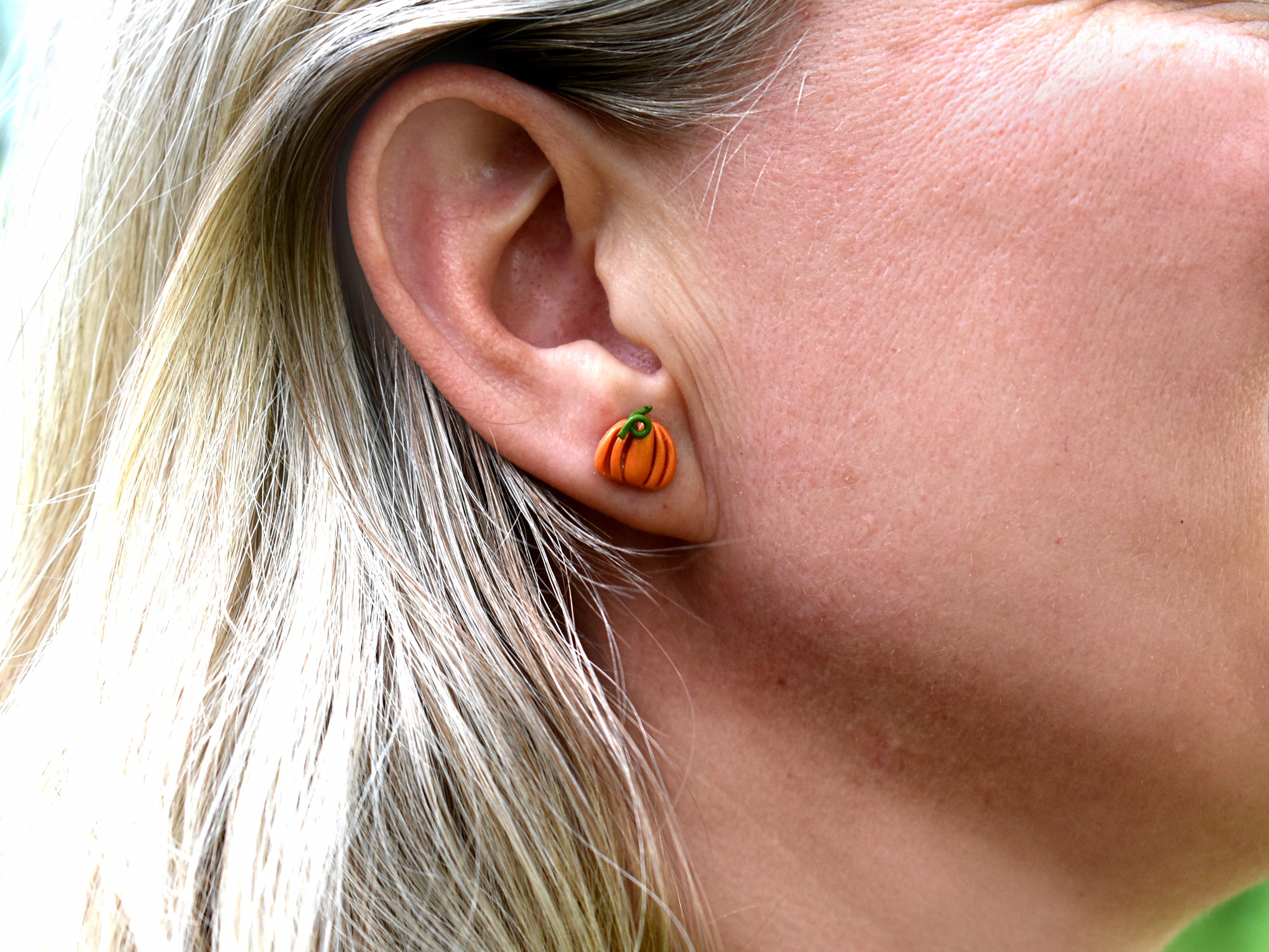 Orange polymer clay pumpkin stud earring worn on the ear, showing the small size and lightweight, understated style of these handmade autumn earrings.