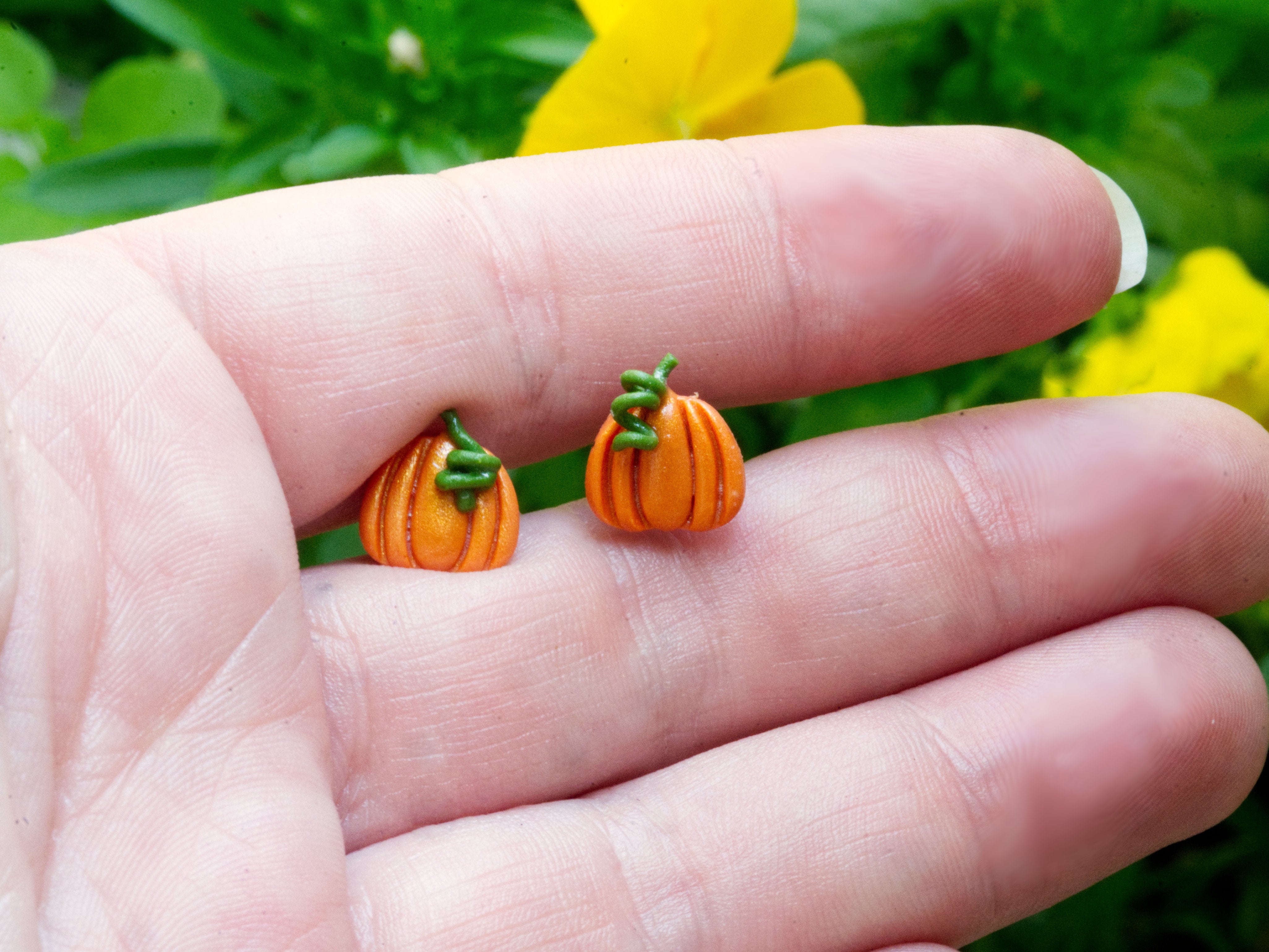 Orange polymer clay pumpkin stud earrings on hand to demonstrate size
