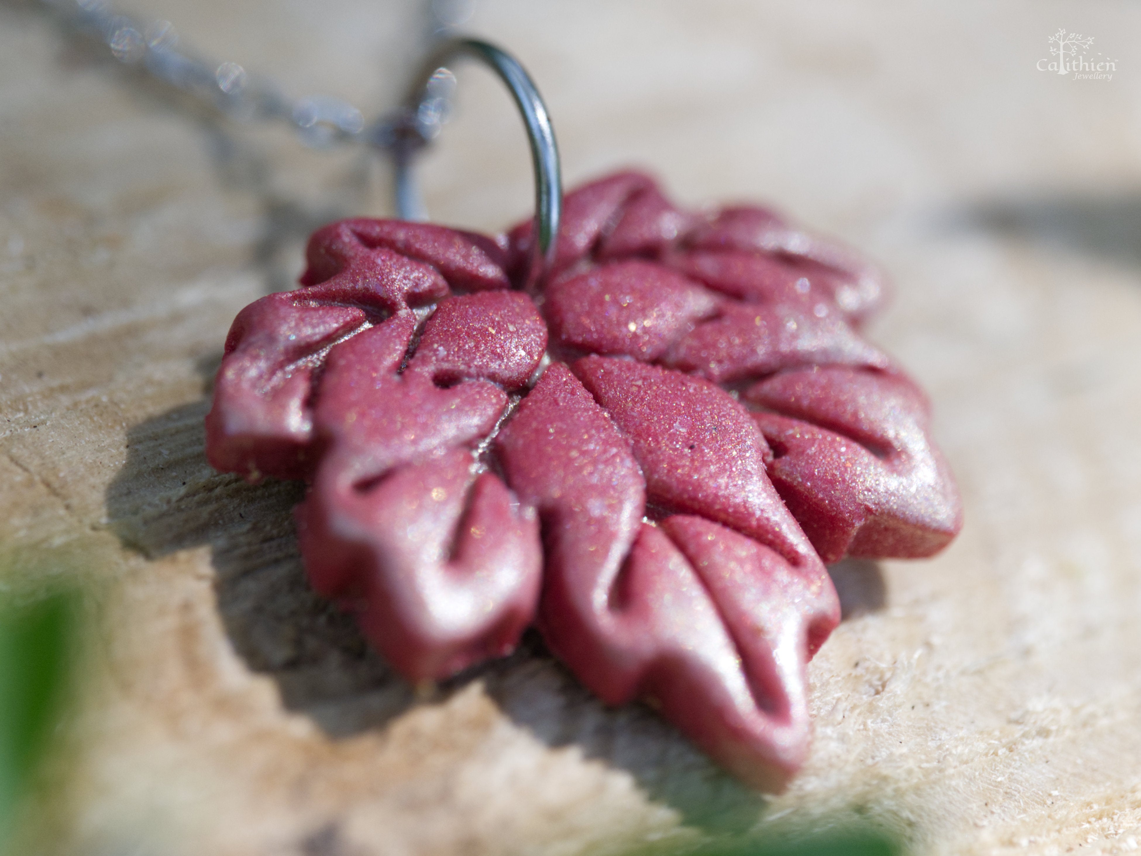 Close-up of red gold shimmer polymer clay maple leaf pendant showing hand-sculpted vein detail and warm light-catching shimmer finish