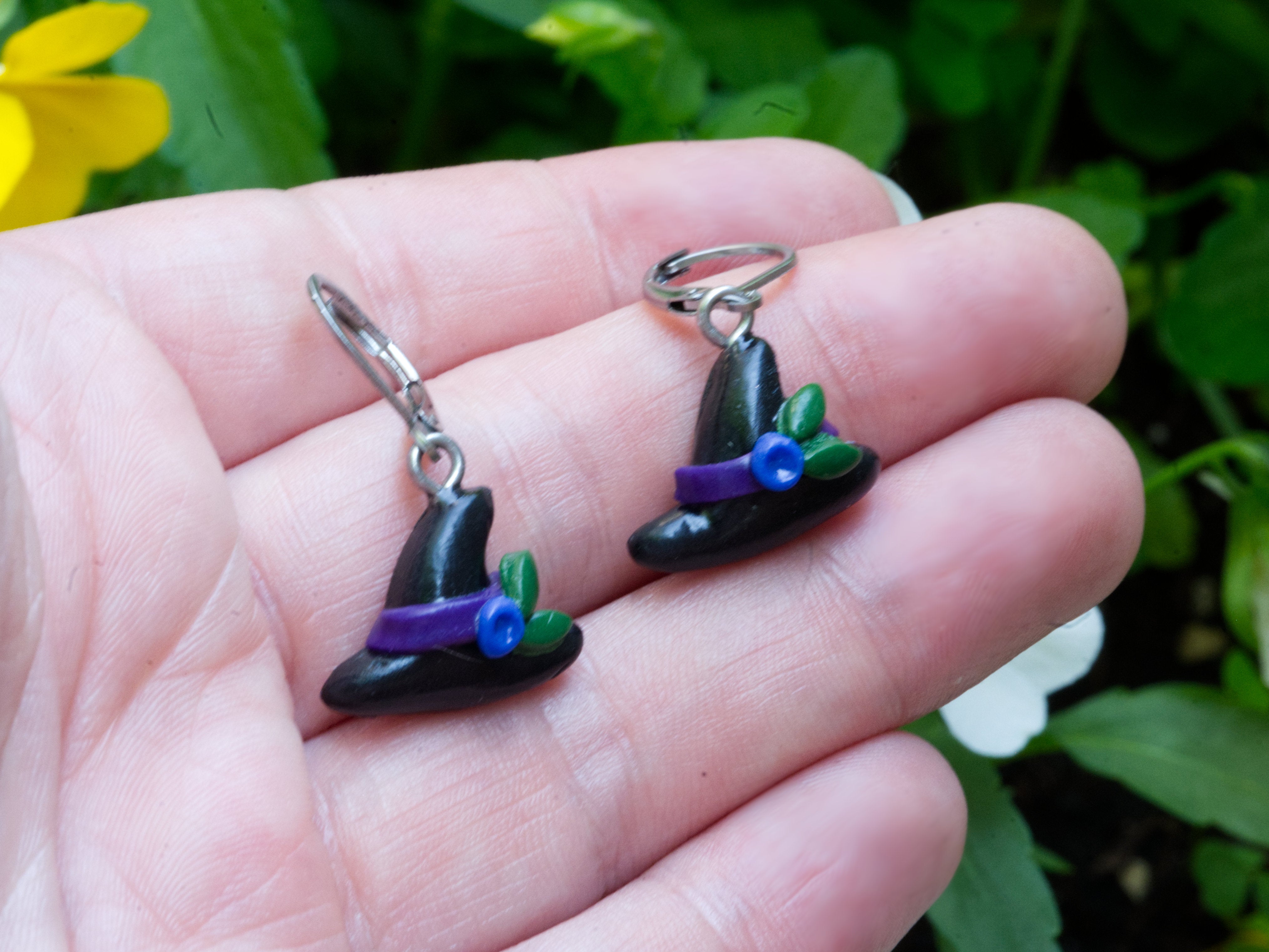 Black polymer clay witch hat earrings on hand to demonstrate size