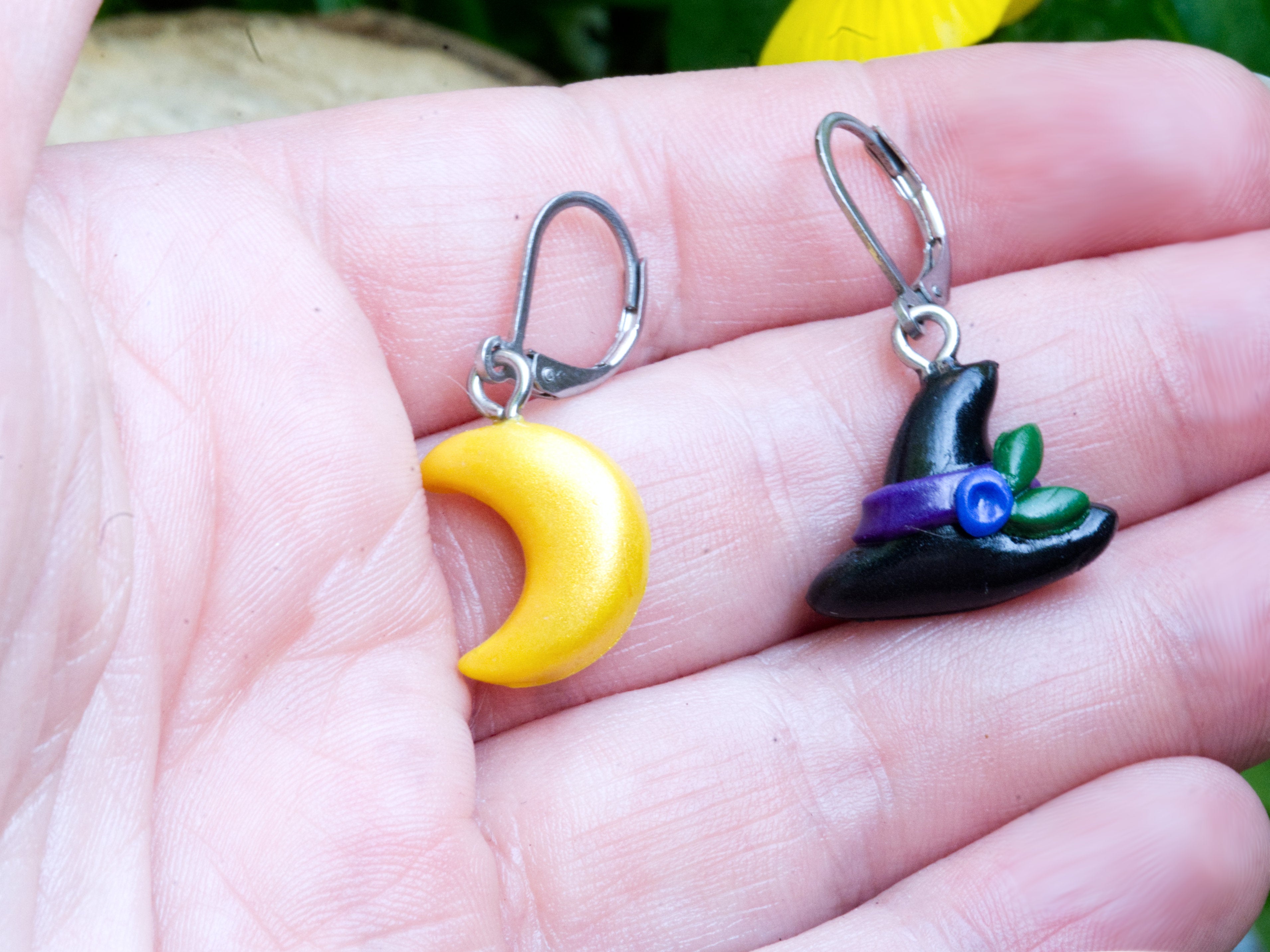 Mismatched witch hat and crescent moon polymer clay earrings at true size on a hand to demonstrate scale