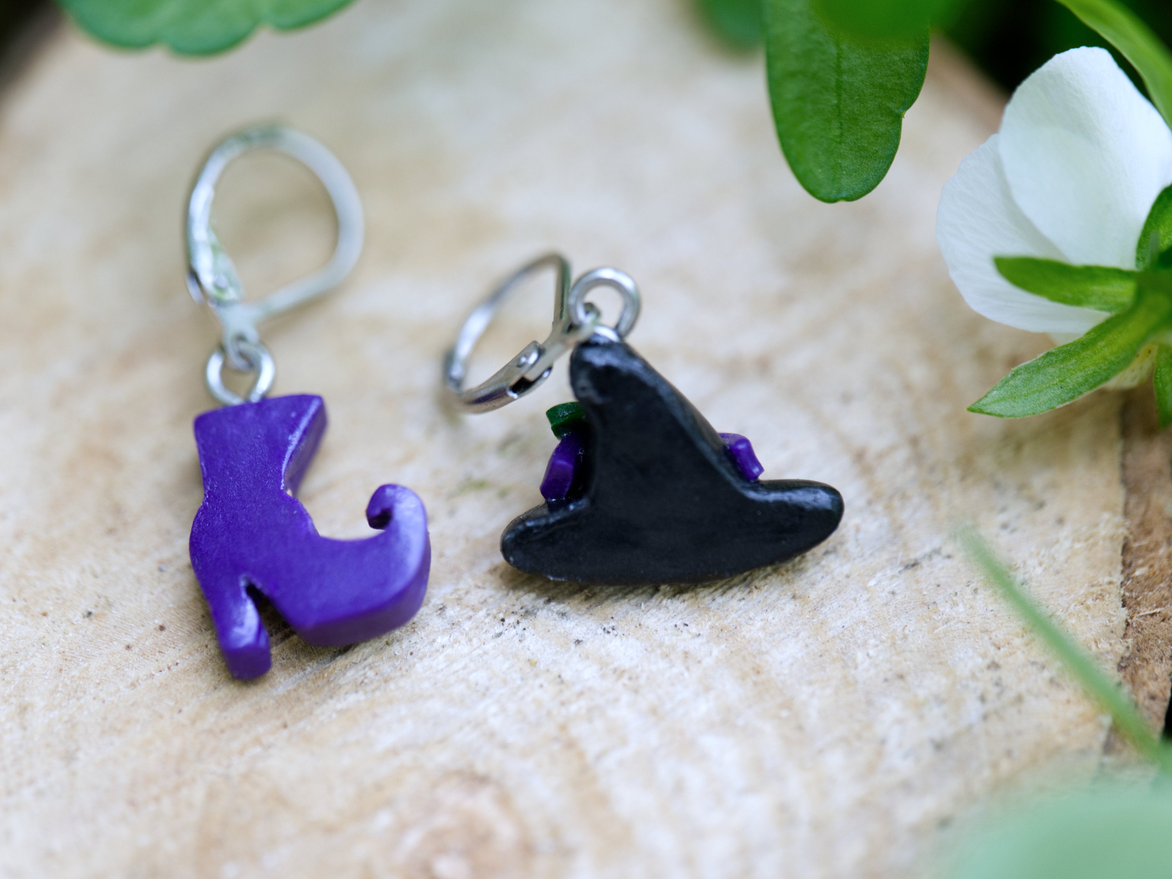 Back of mismatched witch hat earring with purple ribbon and blue flower beside purple polymer clay boot earring with gold buckle detail
