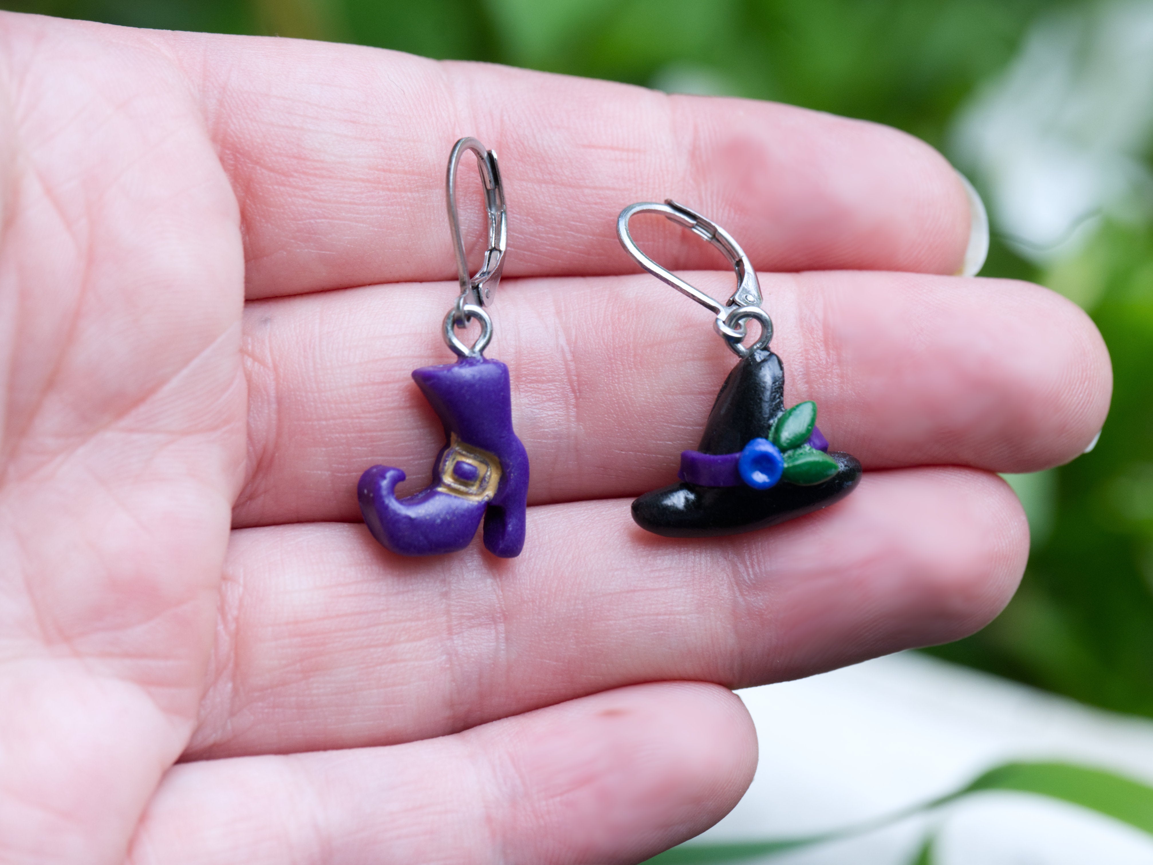 Mismatched witch hat and purple boot polymer clay earrings at true size on a hand to demonstrate scale