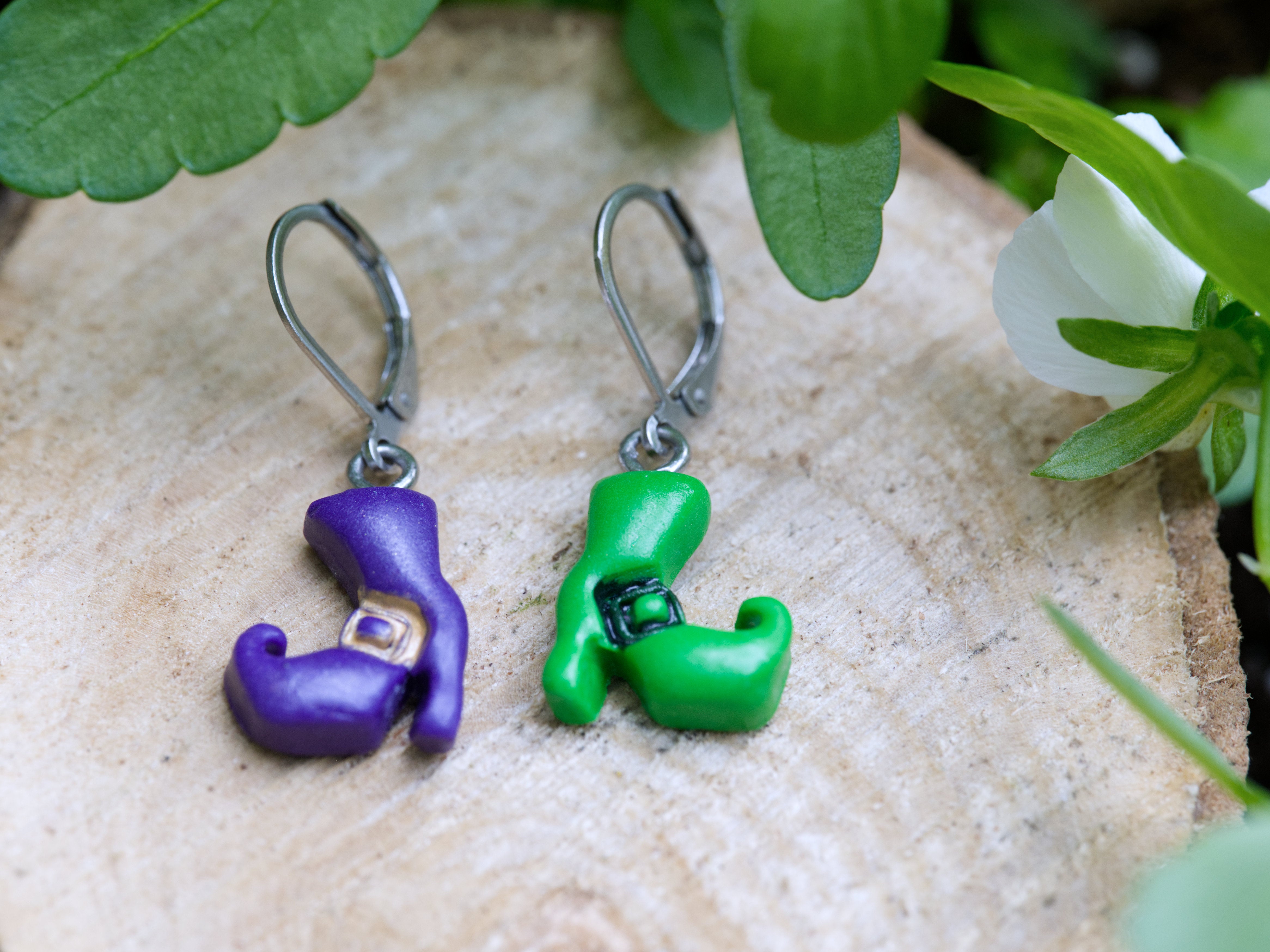 Close-up of mismatched purple and green polymer clay witch boot earring charms showing hand-sculpted buckle detail and curled toes on both boots